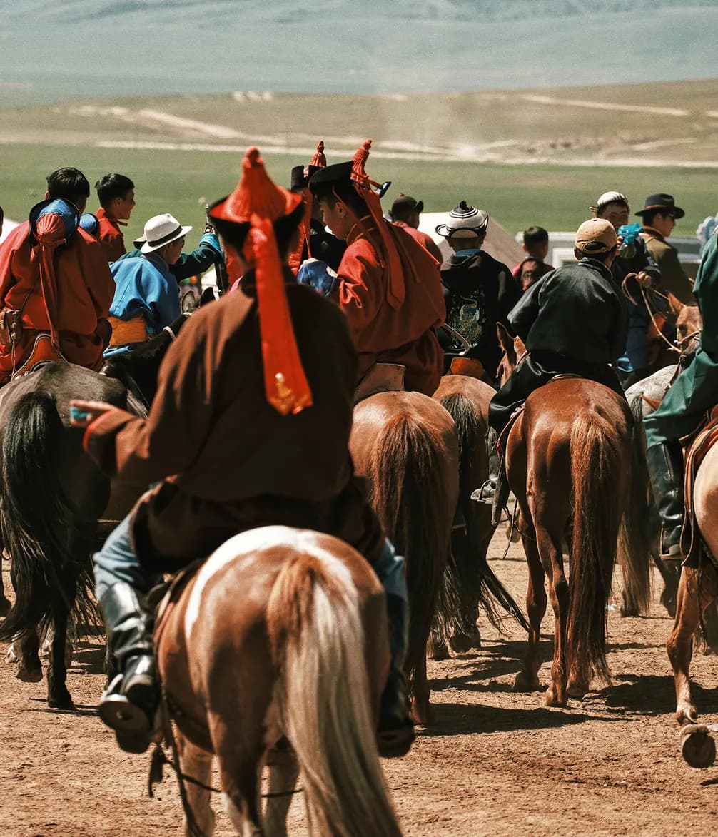 A group of riders in traditional attire on horses gathered outdoors on a grassy plain under a clear sky.