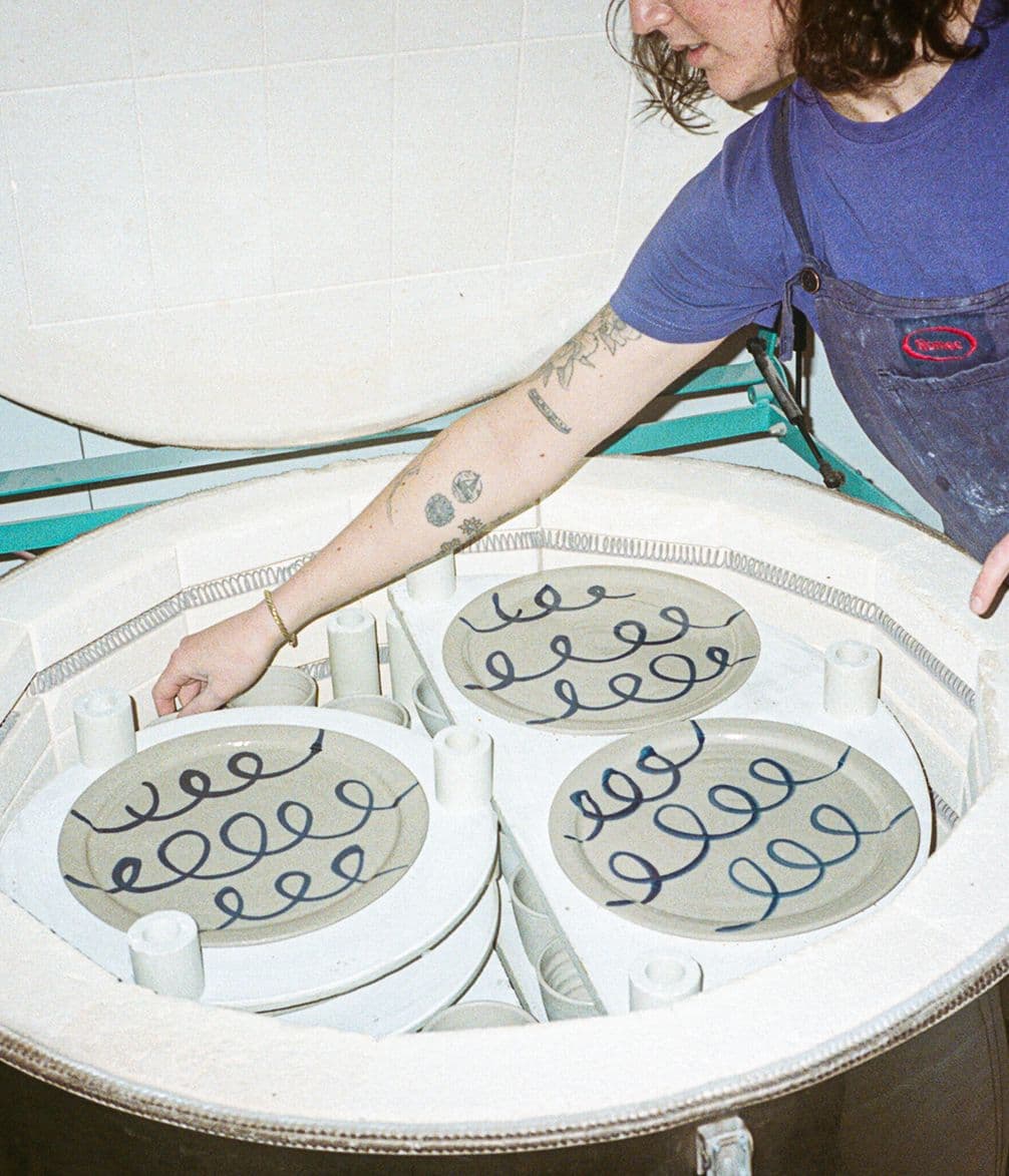 Person placing ceramic plates with blue spiral designs into a kiln.