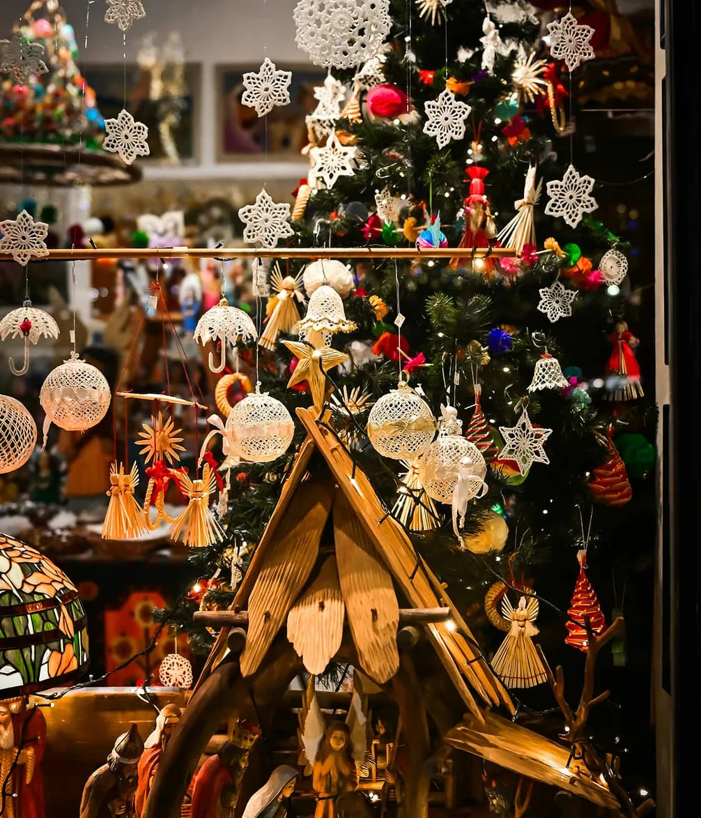 Christmas window display featuring a decorated tree with ornaments and a wooden nativity scene, surrounded by festive hanging stars and lights.