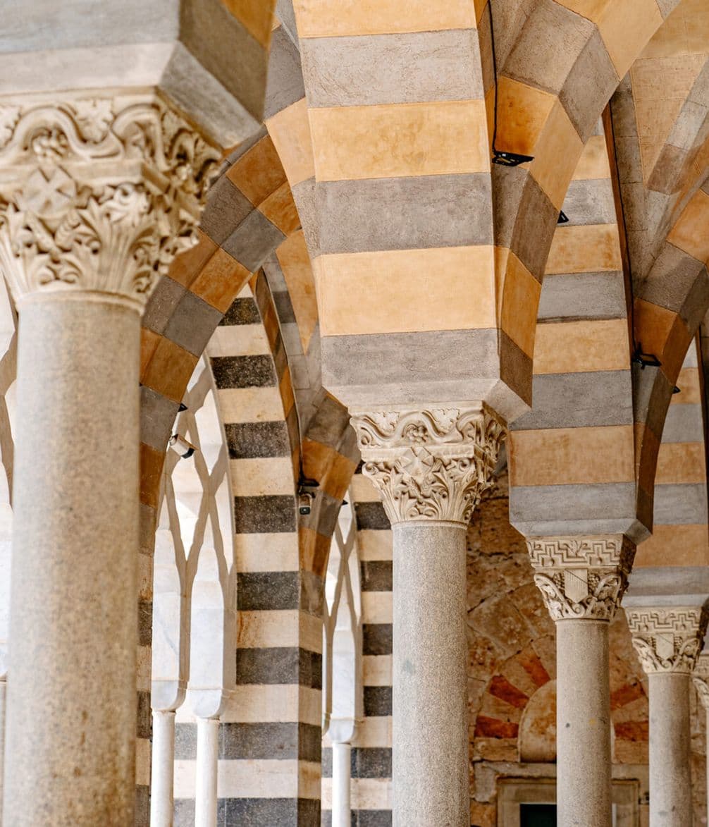 Archway with striped stone and intricately carved capitals on columns, showcasing intricate architectural design and craftsmanship.