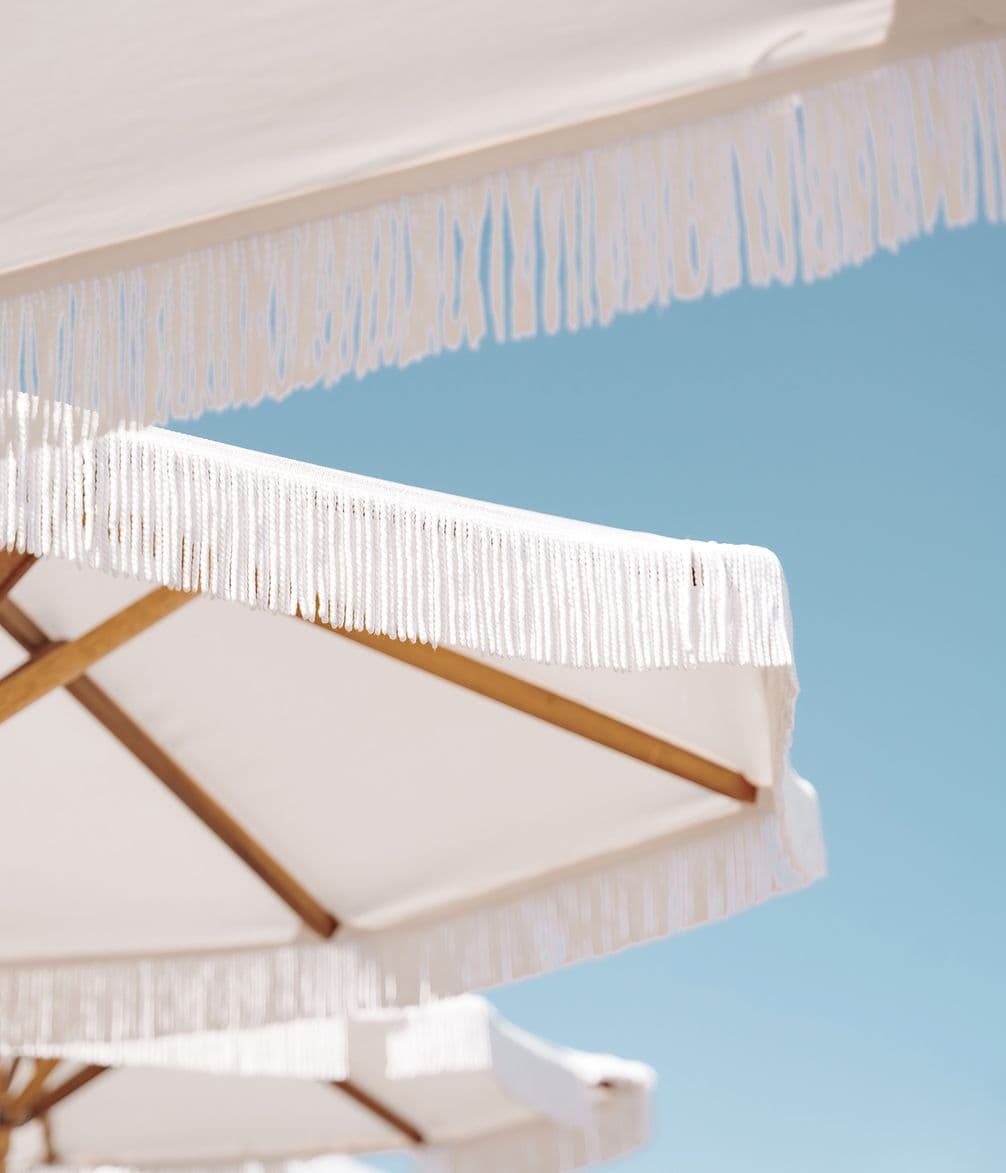 White umbrellas with fringe edges against a clear blue sky.