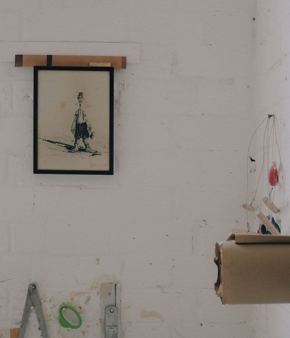 A minimalistic room with a framed sketch of a person on the wall, rolls of paper, and a hanging mobile in view.