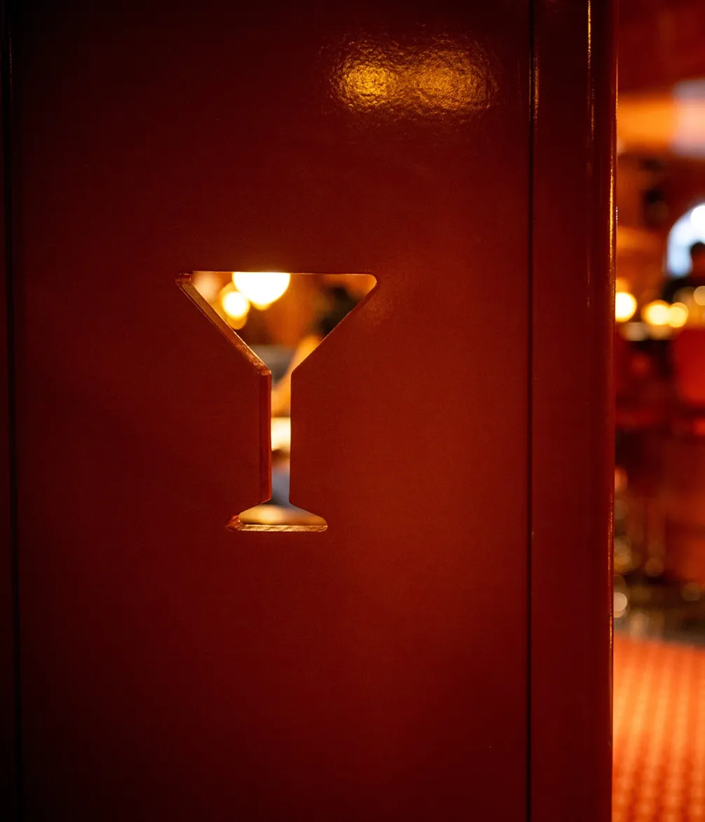 A red wall with a martini glass-shaped cutout, showing warm, ambient lighting in the background.