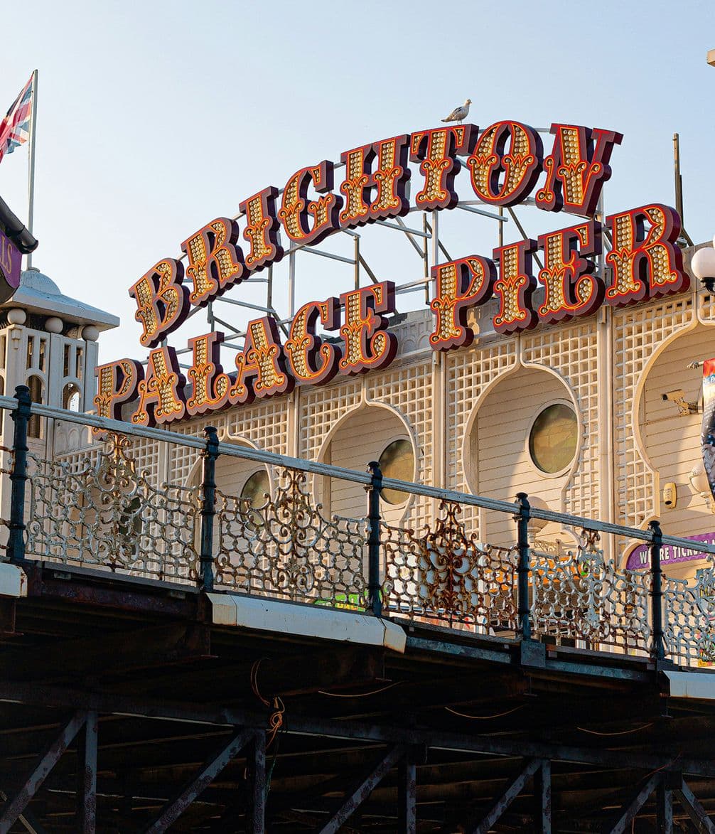 Brighton Palace Pier sign with ornate lettering, surrounded by decorative railing and architecture, under a clear blue sky.