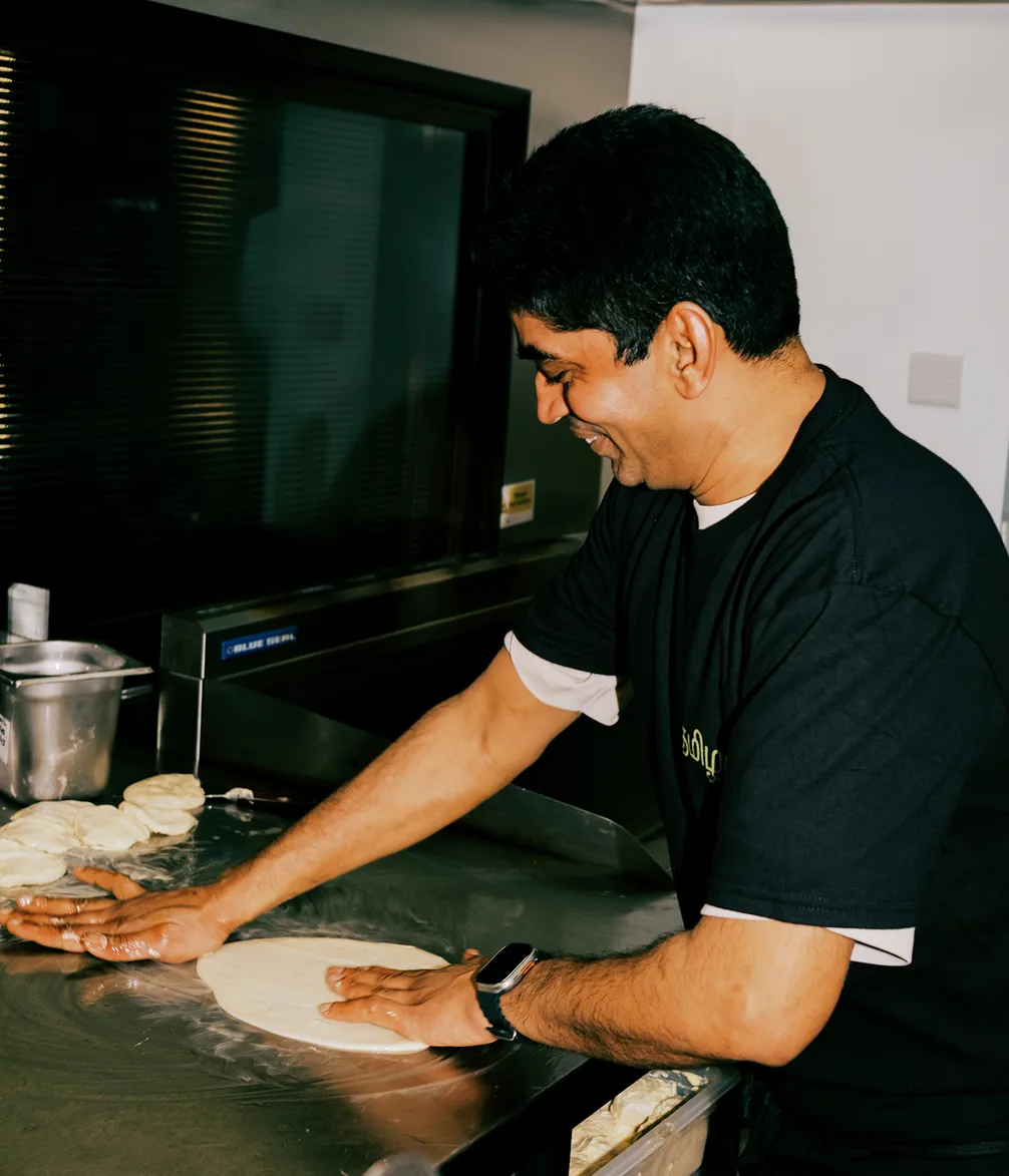 A person wearing a black shirt is joyfully kneading dough on a metal surface in a kitchen.