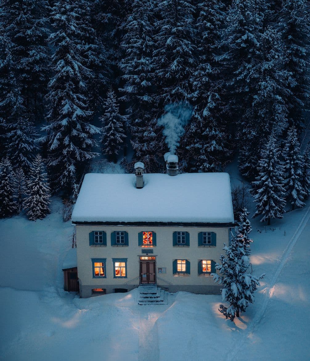 Cottage at night with smoke rising from the chimney and in a snowy landscape