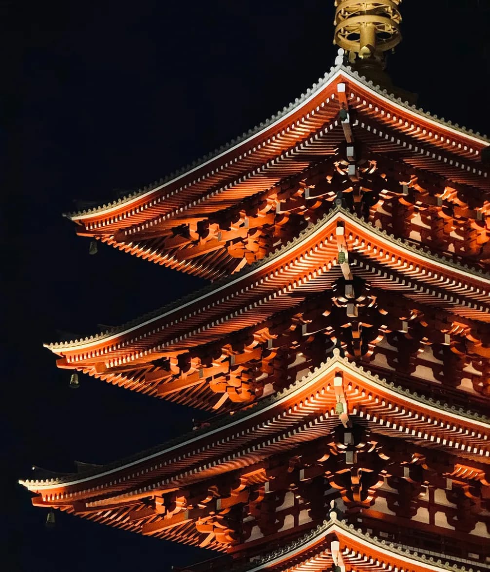 Close-up of a multi-tiered pagoda, illuminated against a dark night sky, showcasing its intricate red and white architectural details.