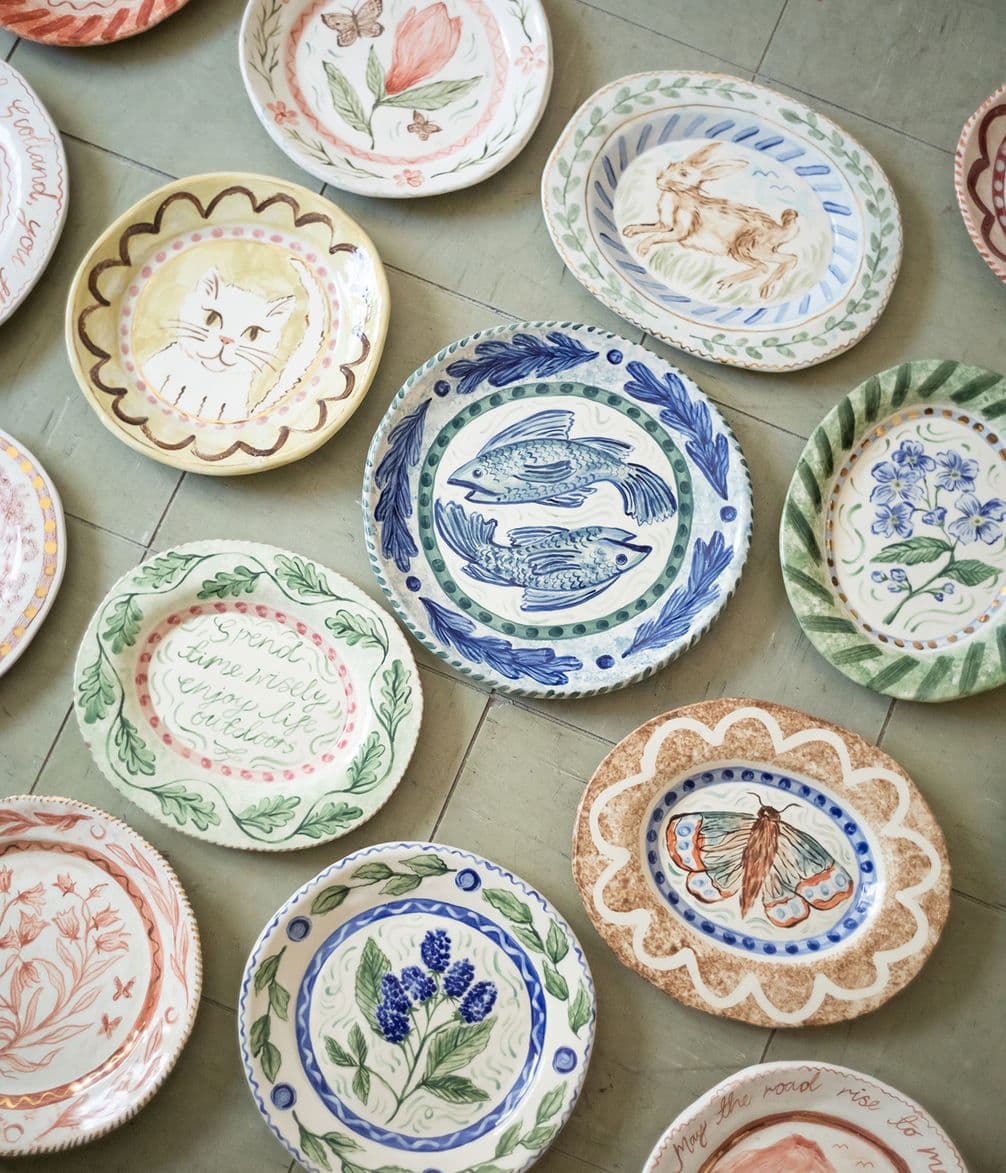 Various decorative ceramic plates with illustrated designs, including flowers, animals, and patterns, arranged on a tiled floor.