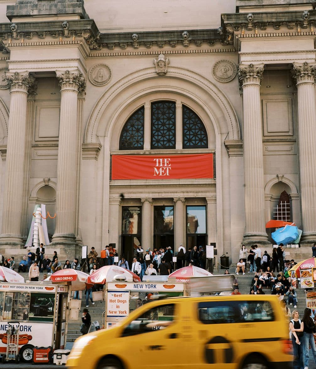 Exterior of The Met in NYC with a yellow taxi and crowds at entrance