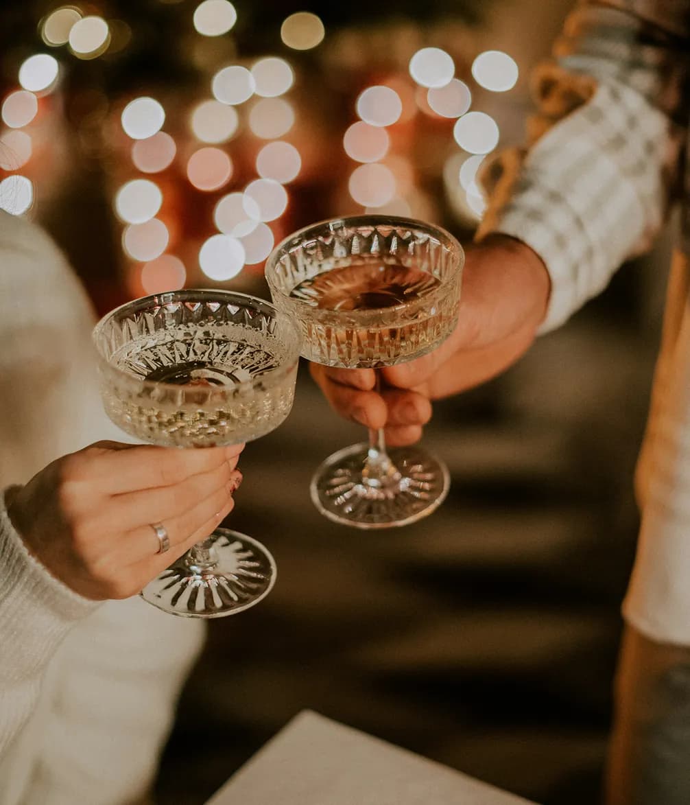 Two people toasting with crystal glasses of champagne, surrounded by festive bokeh lights in the background.