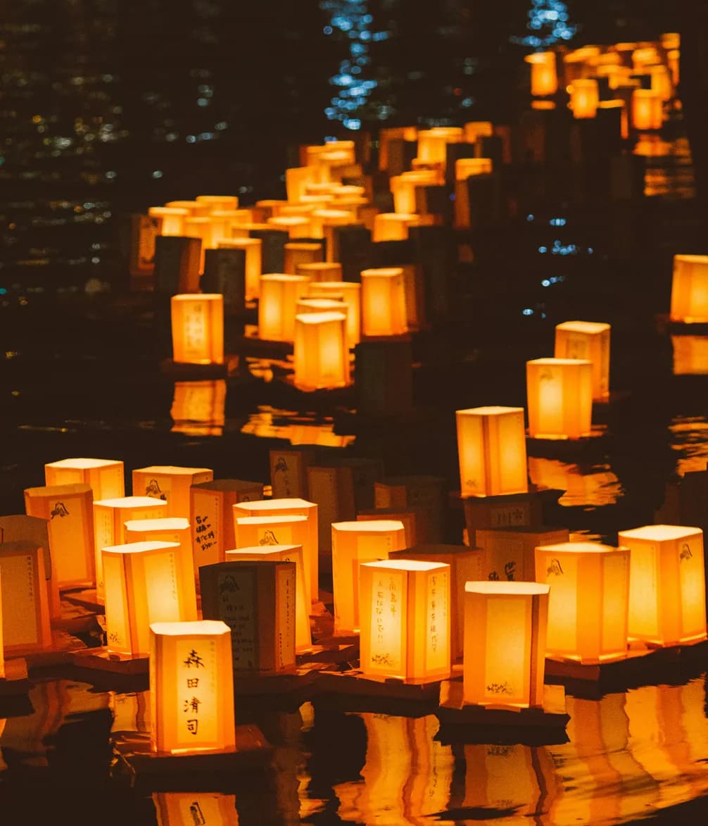 Floating paper lanterns illuminated in warm glow on water, creating a serene and reflective atmosphere during a nighttime festival.