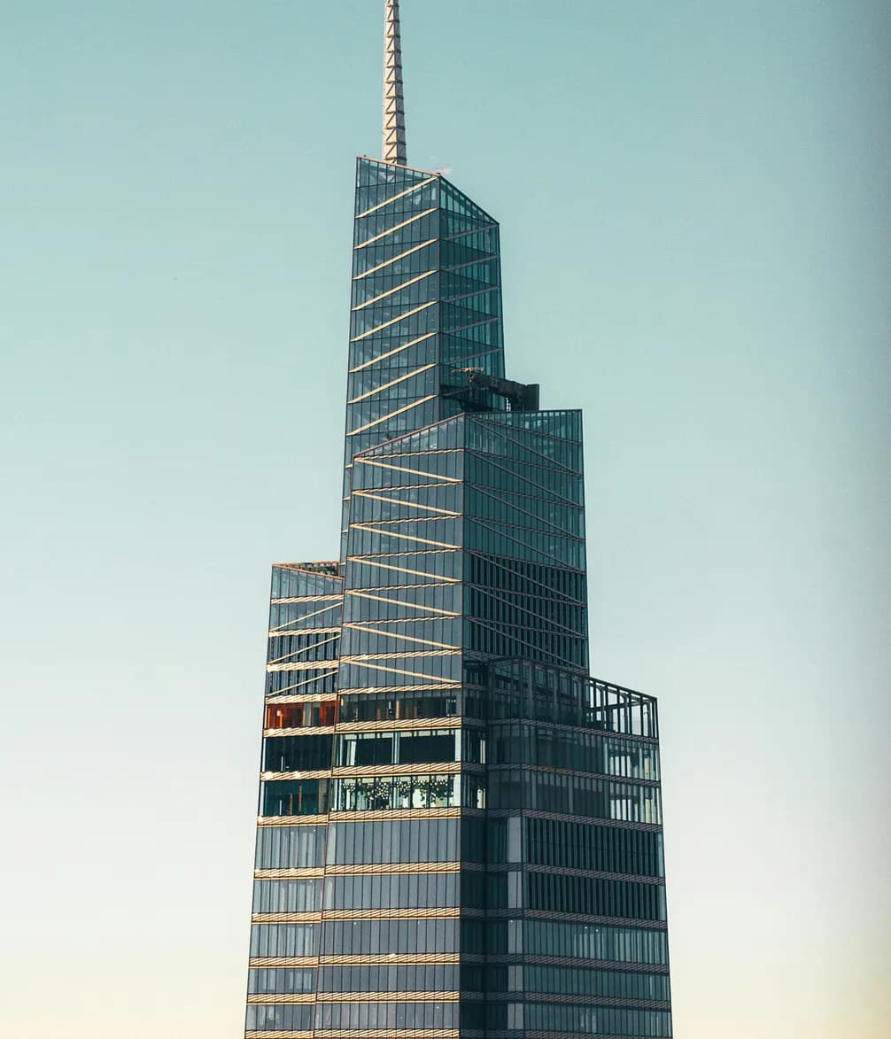 A modern skyscraper with a tapered design and a spire set against a clear blue sky.