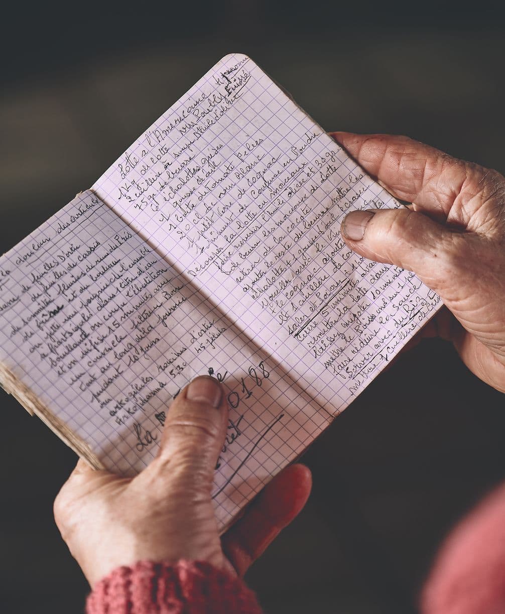 Hands holding an open notebook filled with handwritten text on grid paper.
