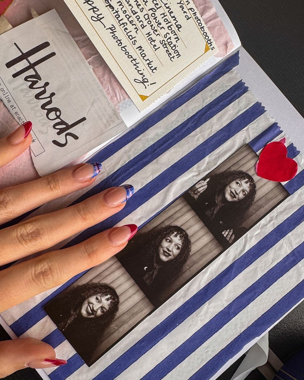 Hand with French-tip nails on blue-and-white striped paper with three-frame black-and-white photo strip, red heart sticker, Harrods tag and note.