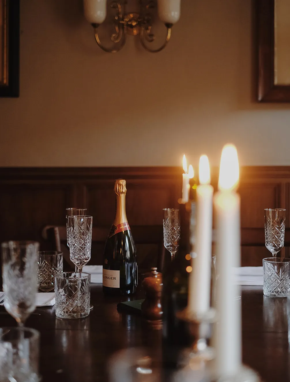 A dimly lit dining table with crystal glasses, a bottle of champagne, and glowing candles creating an elegant and cozy atmosphere.