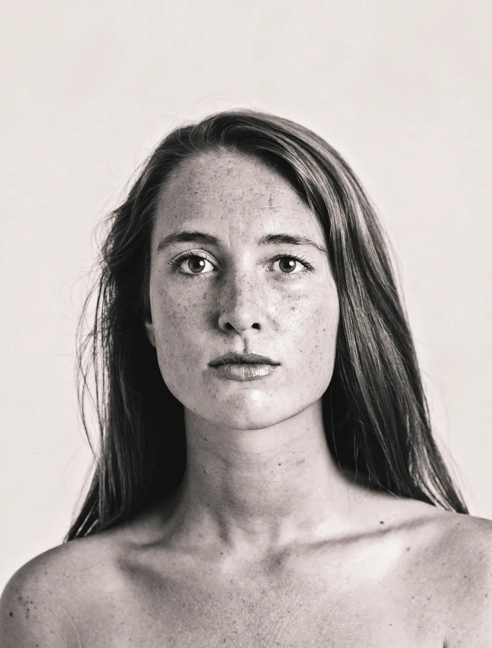 A woman with long hair and freckles, gazing directly at the camera in a black and white portrait with a neutral expression.