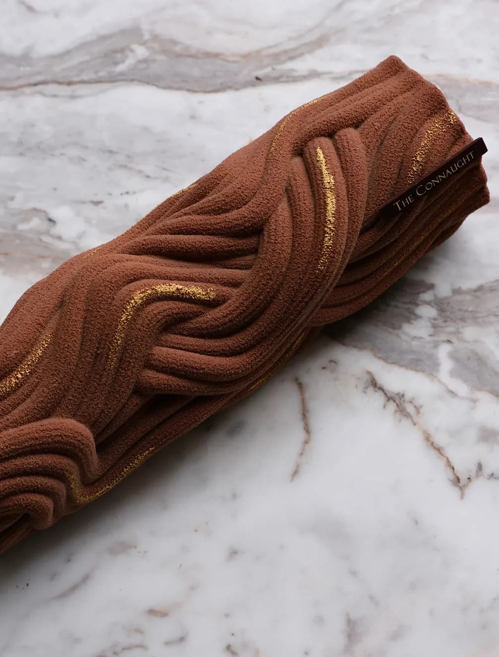 A chocolate dessert with textured wavy patterns and gold accents, labeled "The Connaught," on a marble surface.