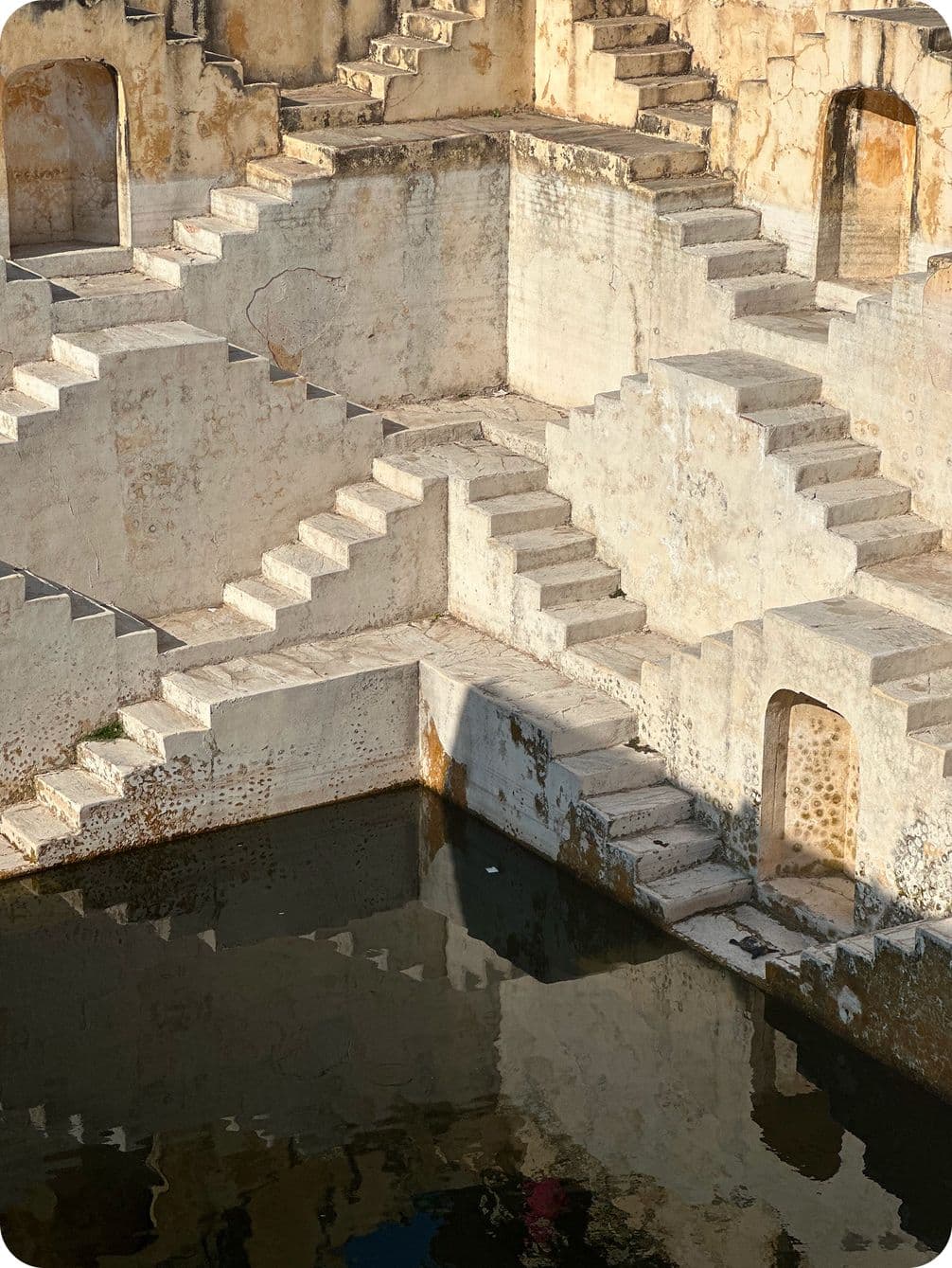 Ancient stepwell with symmetrical, crisscrossing stone staircases leading to a pool of water, showcasing intricate architectural design.