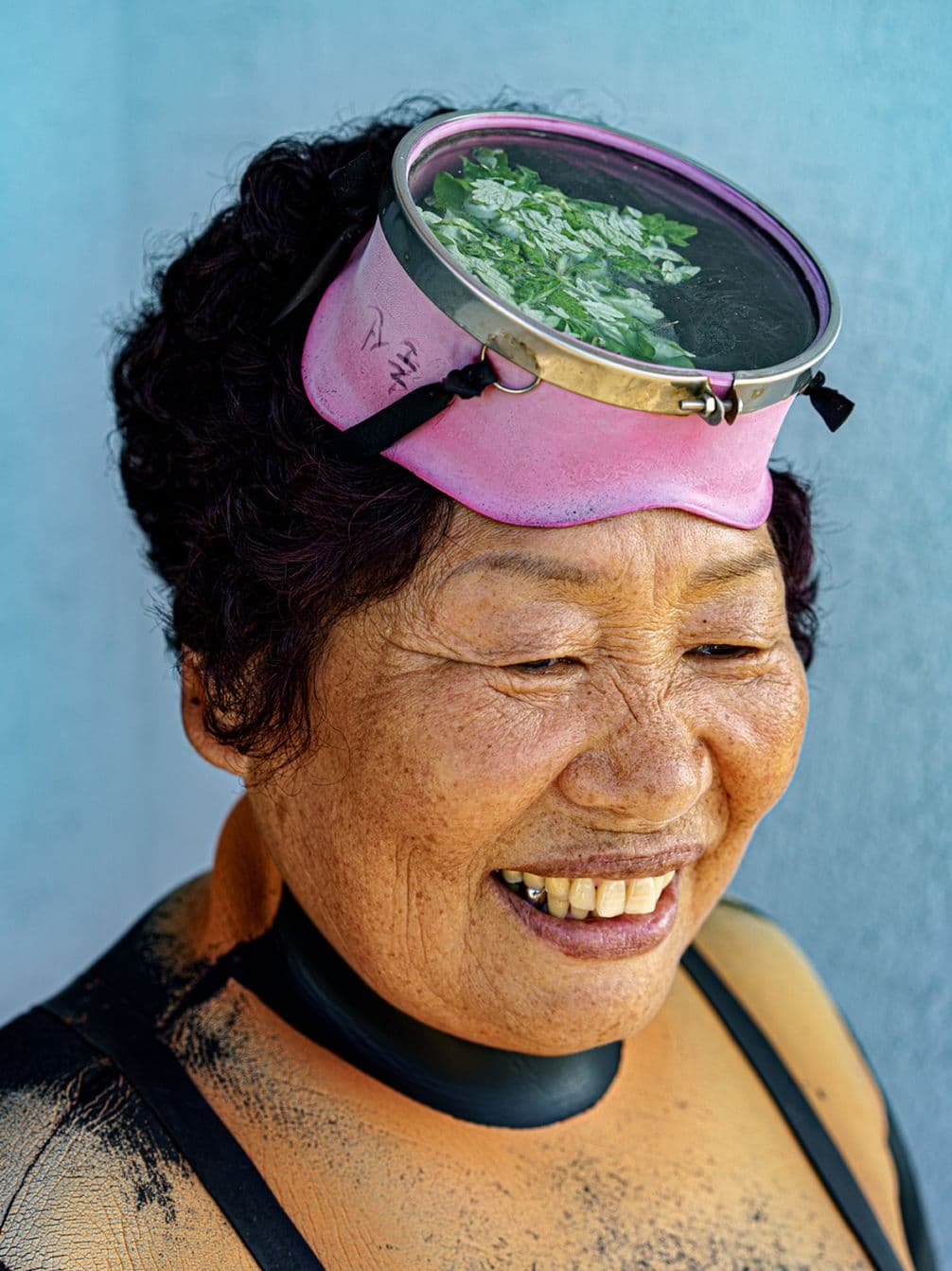 Smiling woman with a snorkeling mask on her head, wearing a wetsuit, against a blue background.