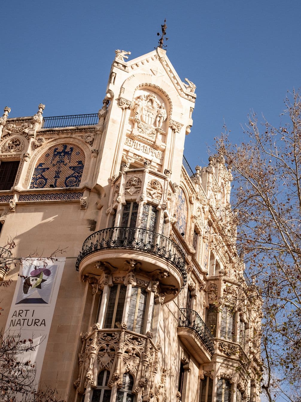 Ornate historic building with intricate carvings and balconies under a clear blue sky, featuring a banner reading "Art i Natura."
