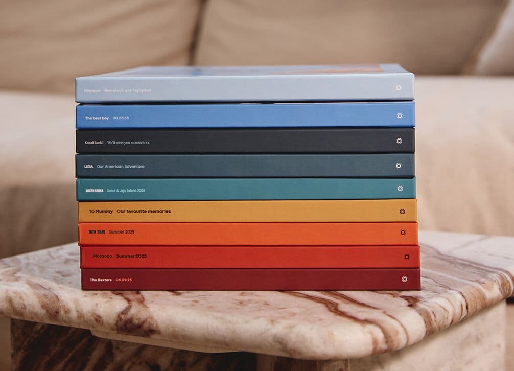 A stack of colorful books with white text on the spines, resting on a marbled table in front of a beige couch.