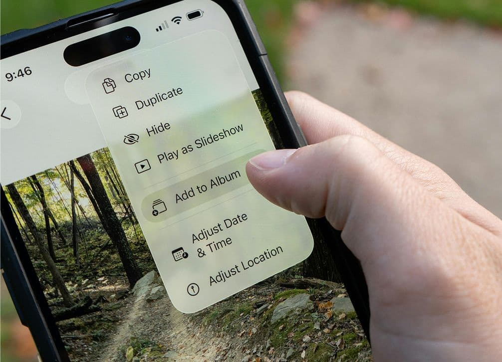 Close-up of a hand holding a smartphone, displaying photo editing options over an image of a forest trail on the screen.