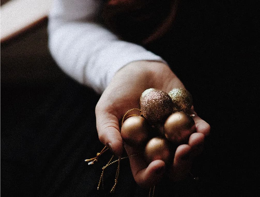 A hand holding several small, glittery Christmas ornaments in shades of gold and bronze.
