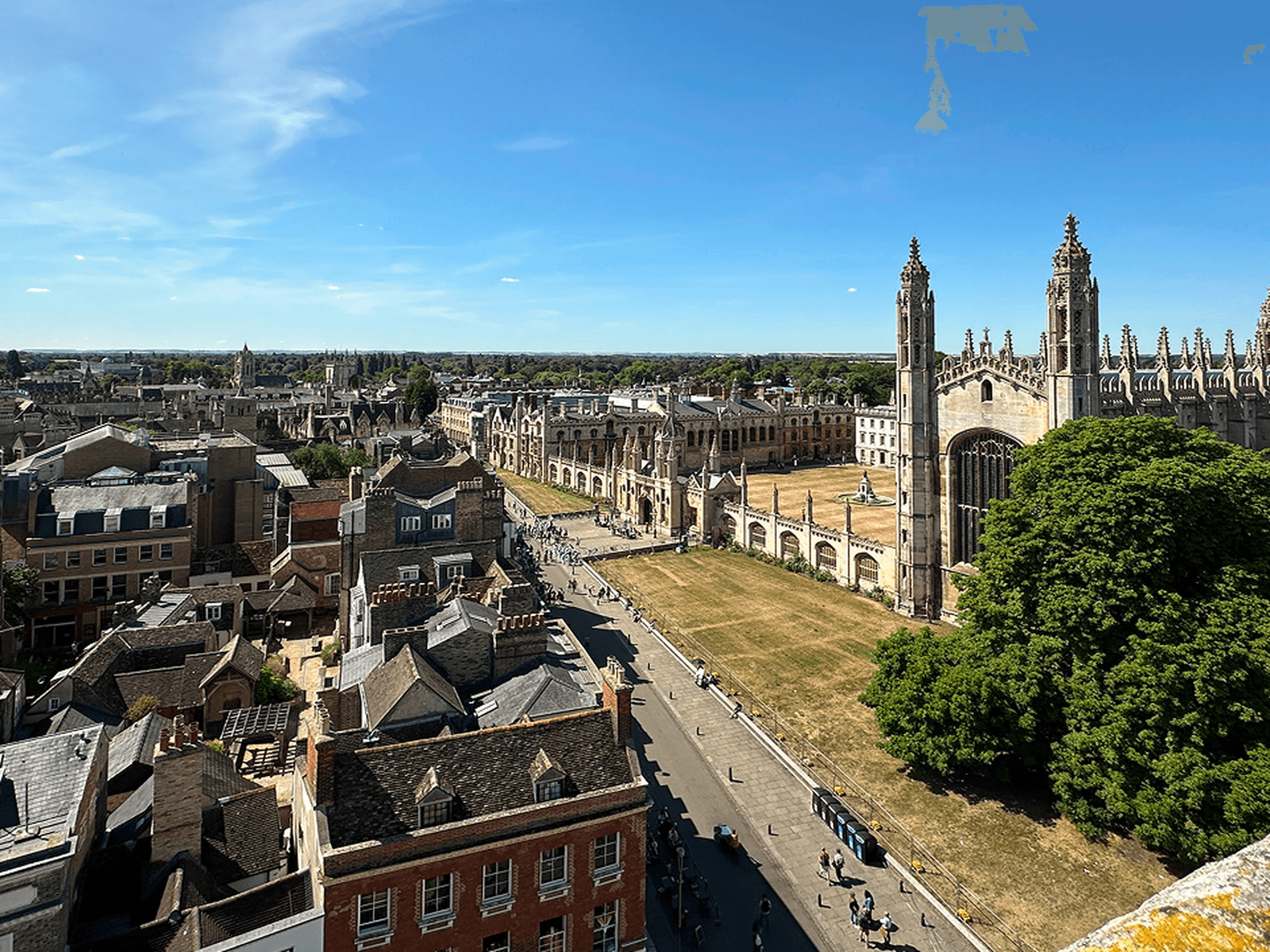 Aerial view of a historic city with a large Gothic-style building, tree-lined streets, and a clear blue sky.