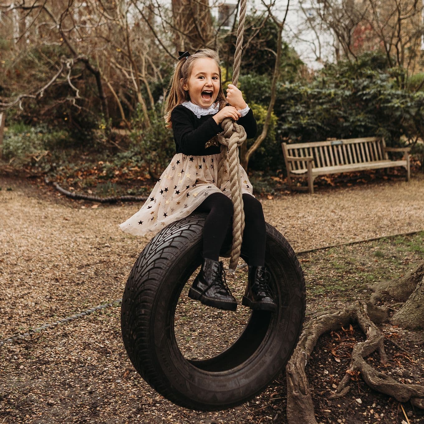 Schoolgirl smiles open mouthed while sat on a tyre swing