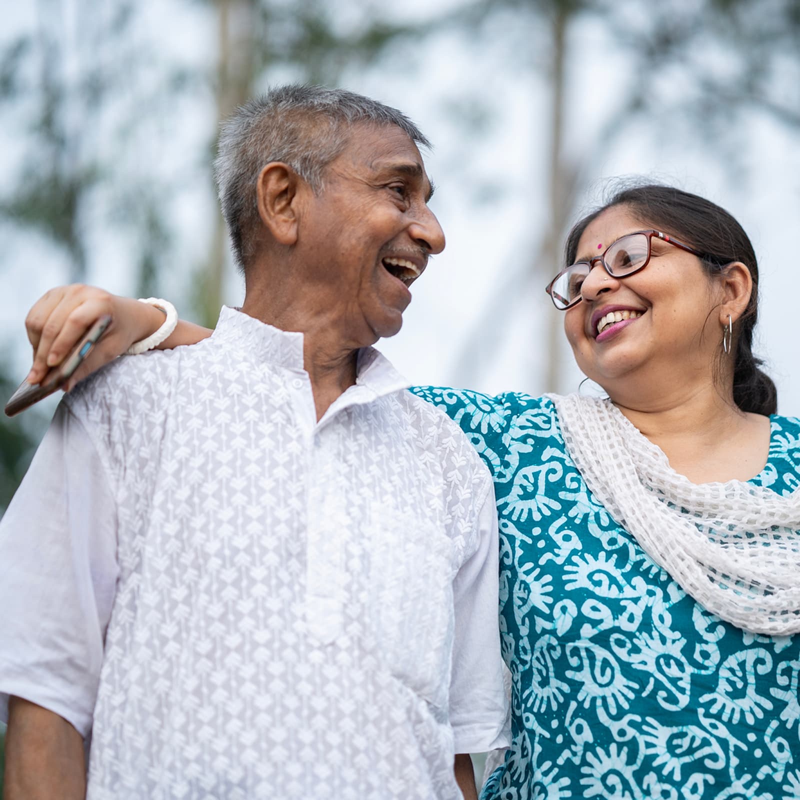 An adult daughter embraces her father while holding a mobile phone