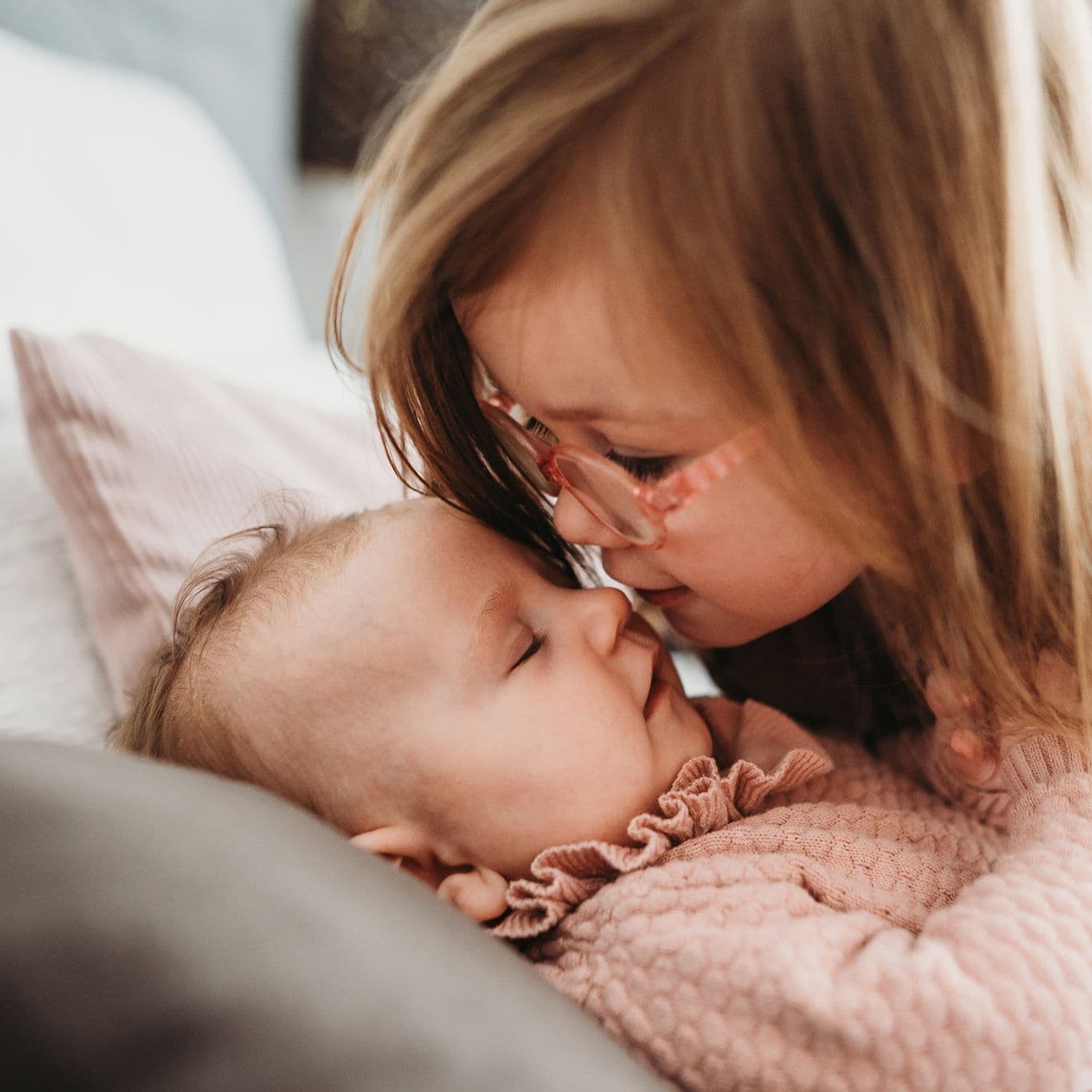 A preschool-age girl leaning over kissing her baby sister's nose
