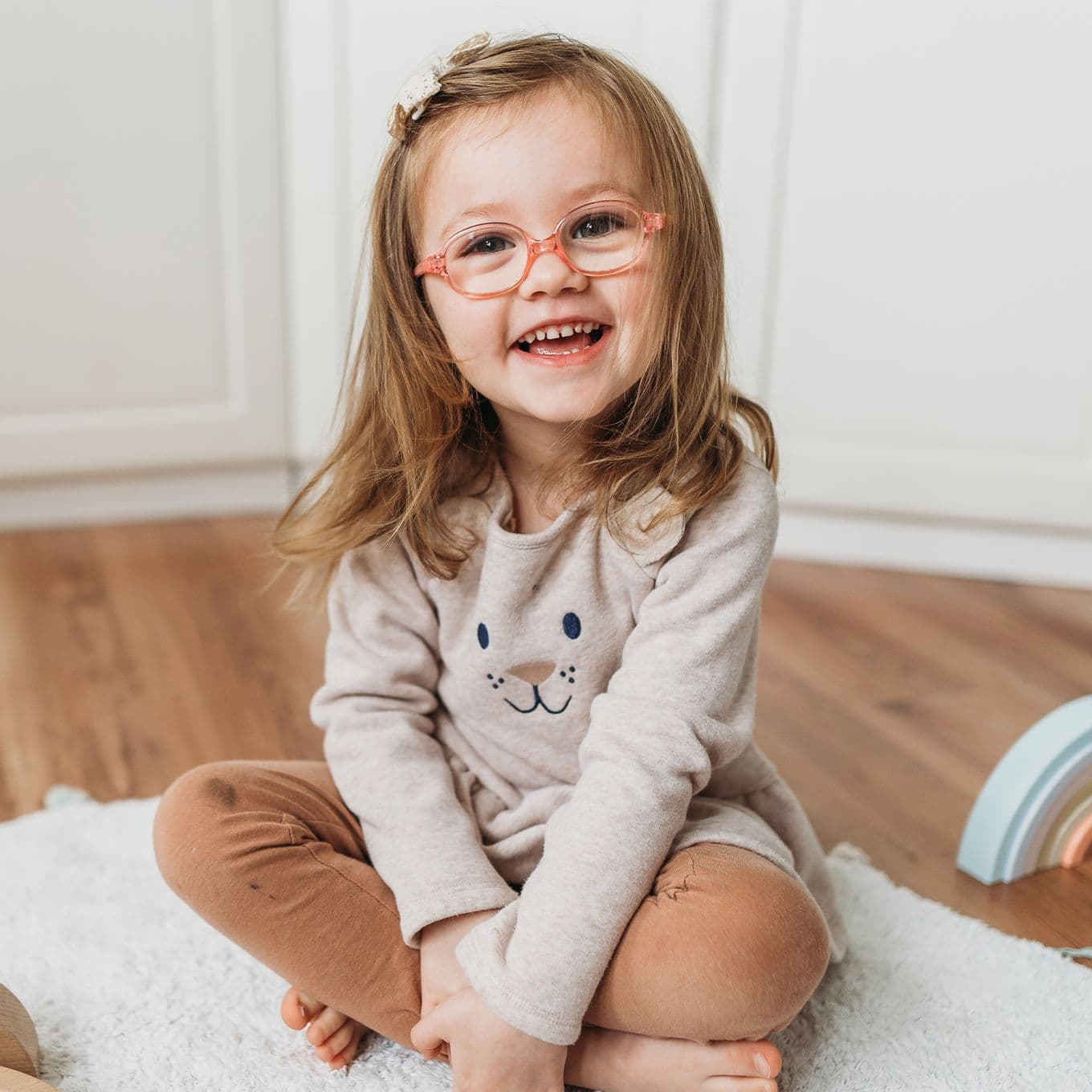 Preschool-age girl smiles at the camera while sitting cross legged on a rug