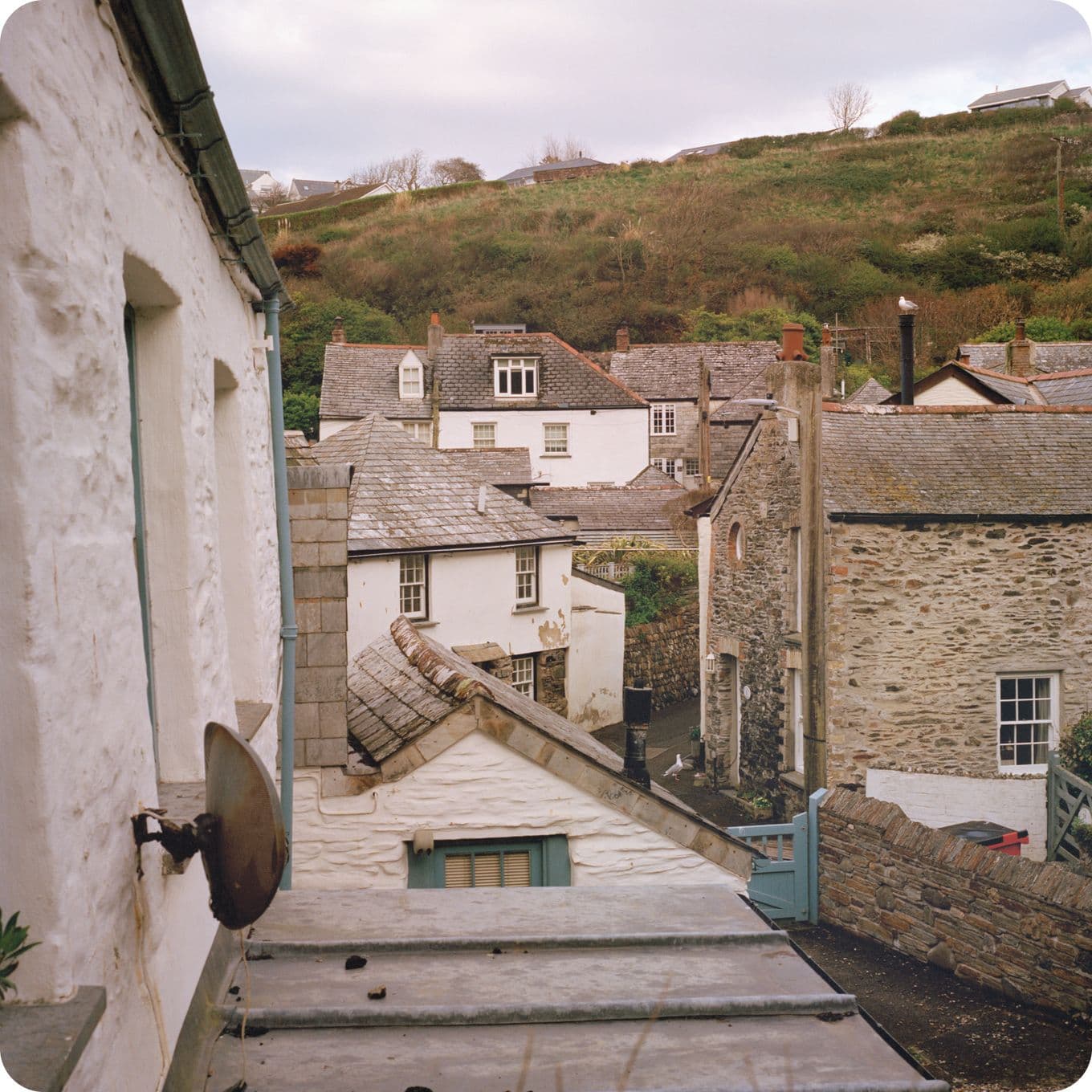 A quaint village scene with stone cottages, slate roofs, and a hilly backdrop under a cloudy sky.