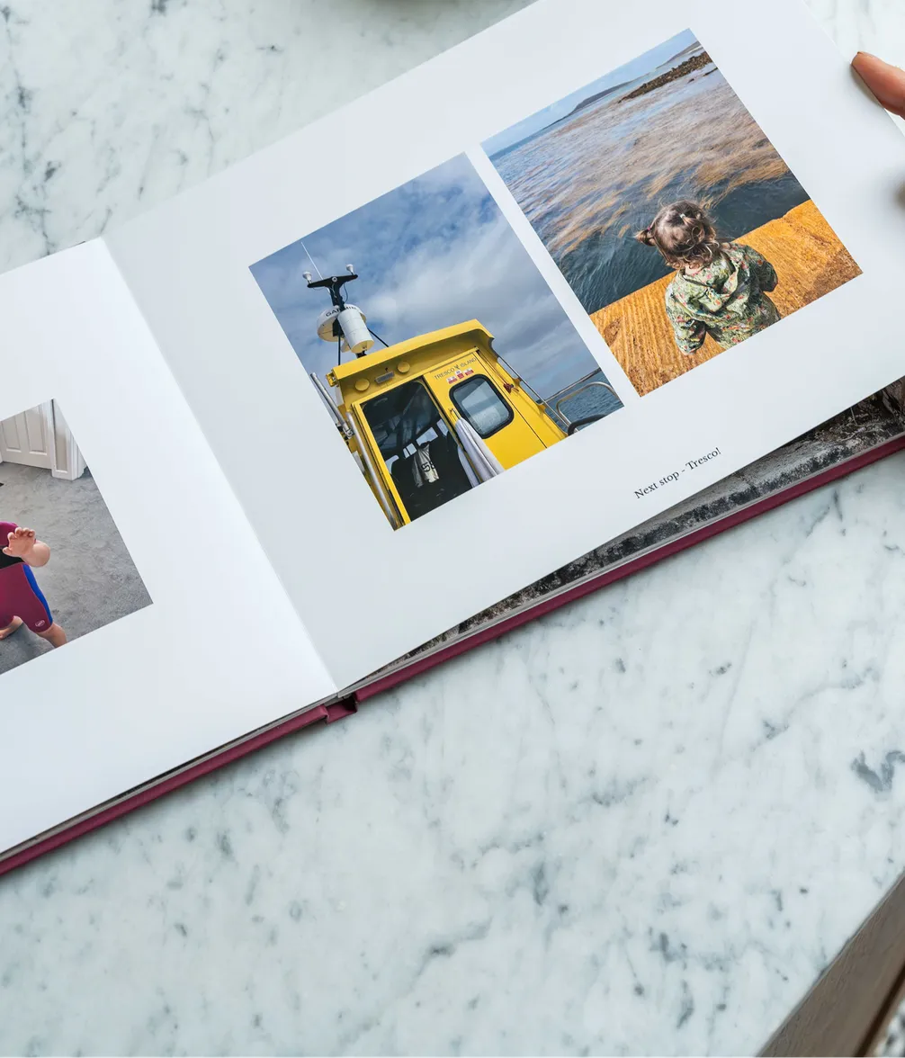 Open photo book on a marble surface showing images of a yellow boat and a child by the sea.
