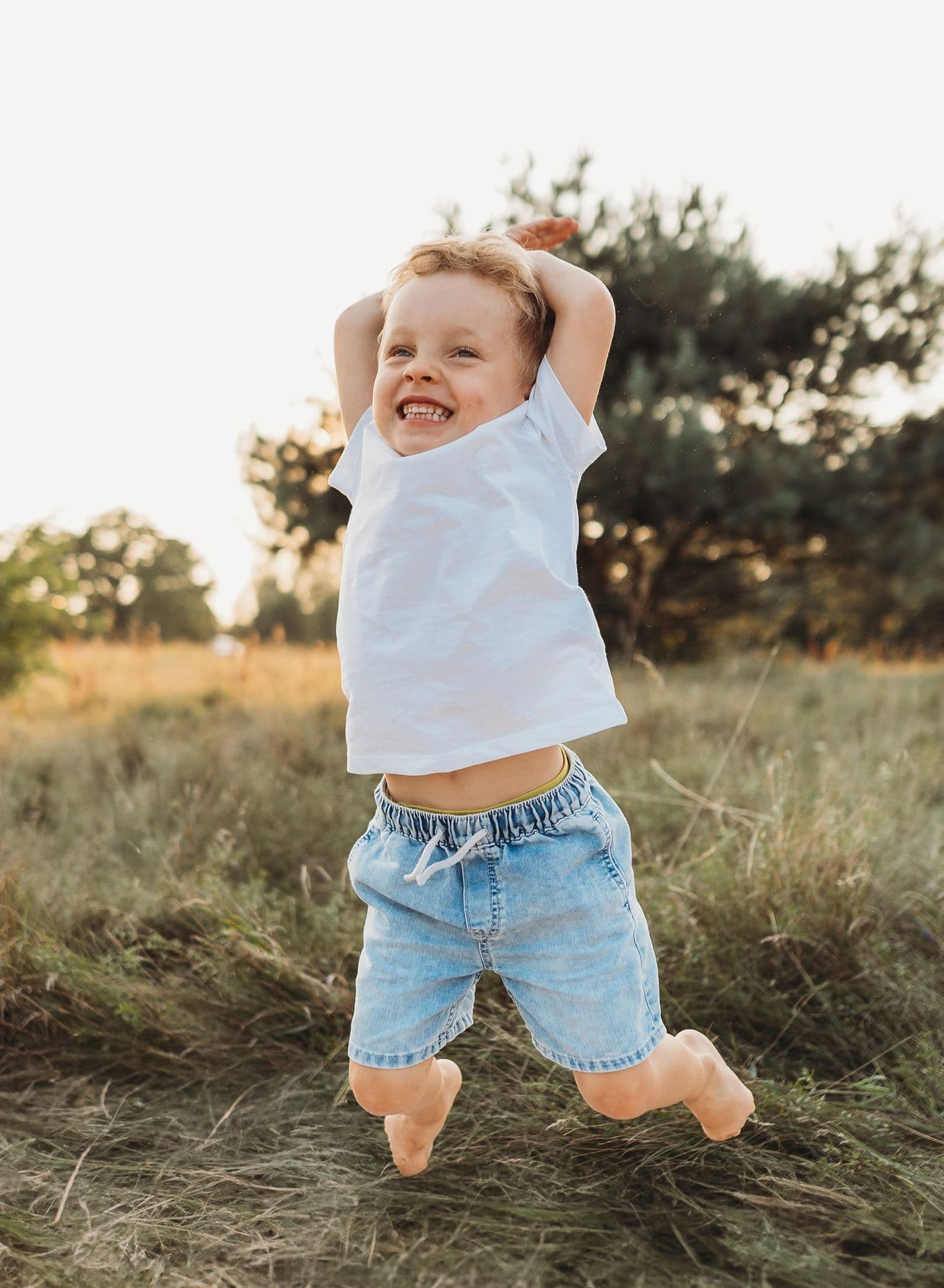 A young boy jumps for joy barefoot in a field