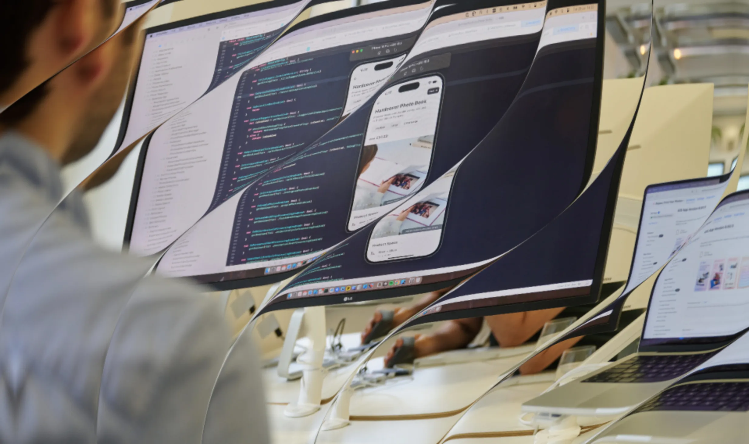 Distorted view of a person working on a monitor showing code and a mobile app preview, with a laptop displaying app listings nearby.