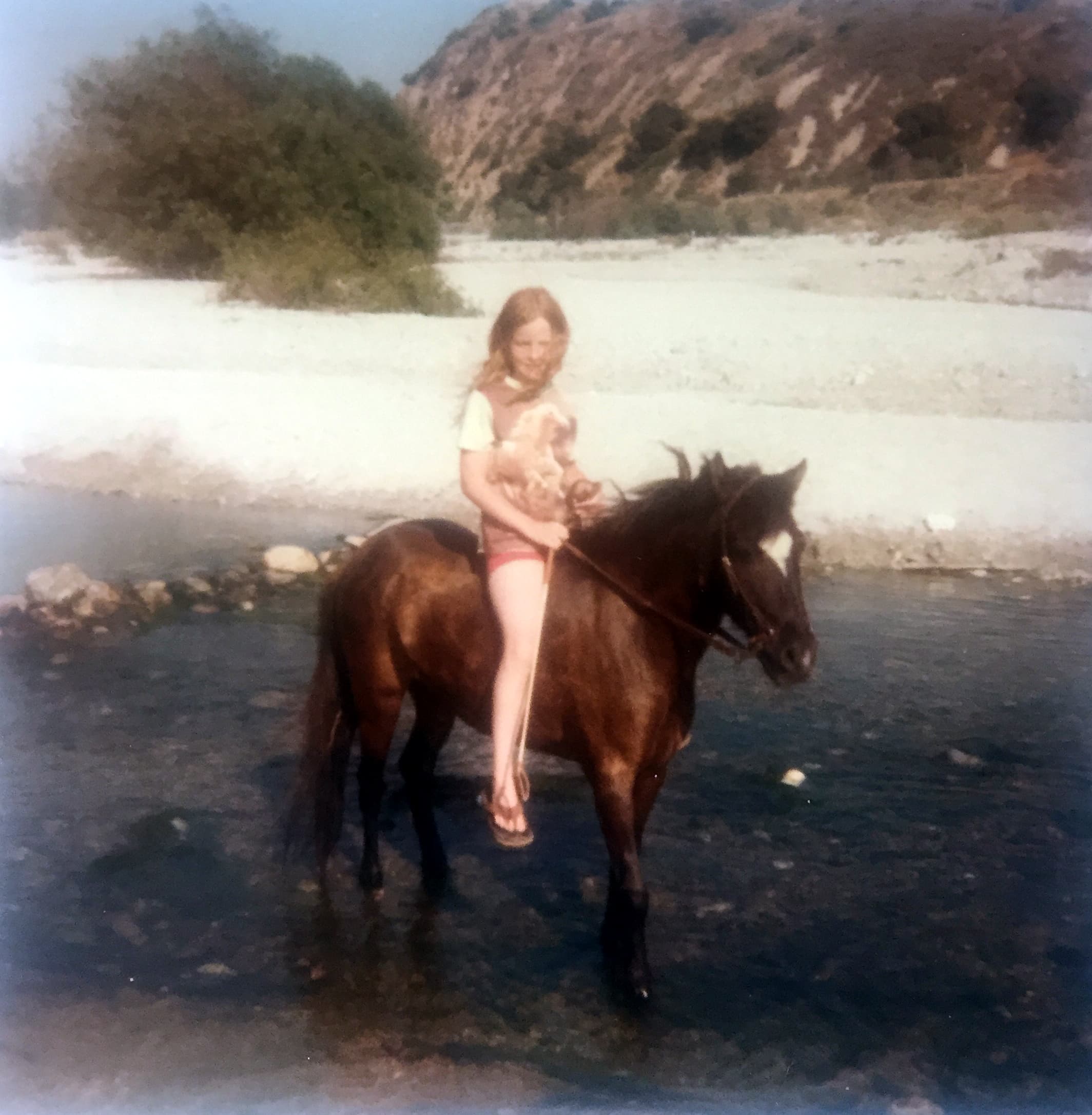 A young Staci Layne Wilson riding her pony, Smokey, through shallow streams