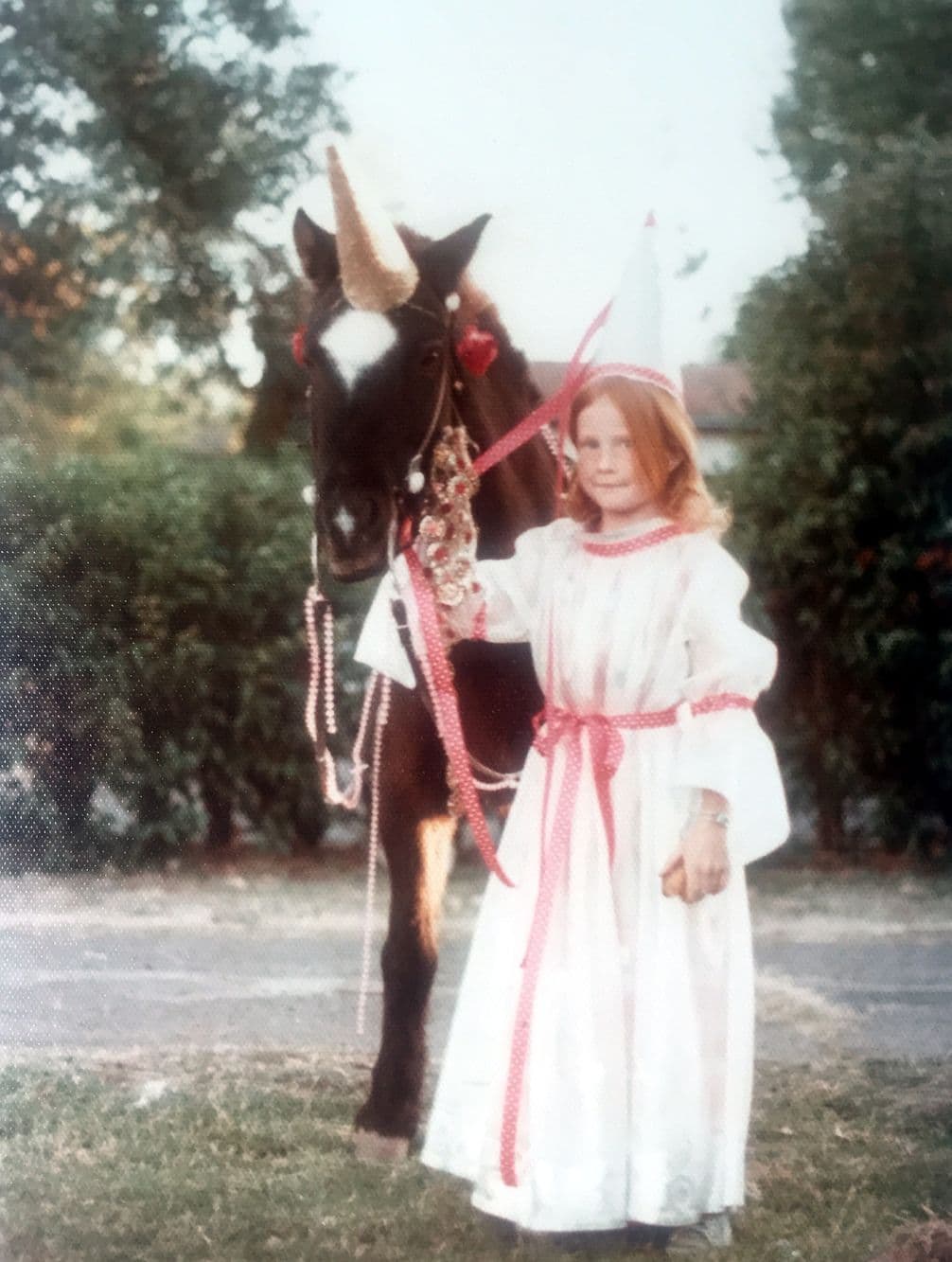 A young Staci Layne Wilson in fancy dress holding the reigns of her pony, Smokey, dressed up like a unicorn