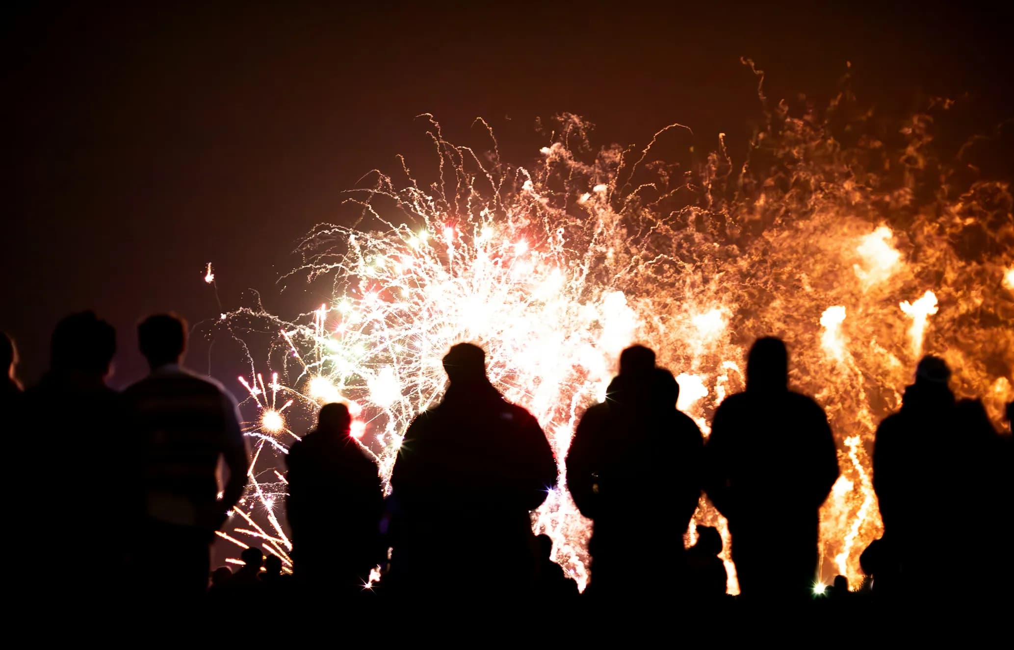 Silhouetted people watching a vibrant fireworks display against a dark night sky.