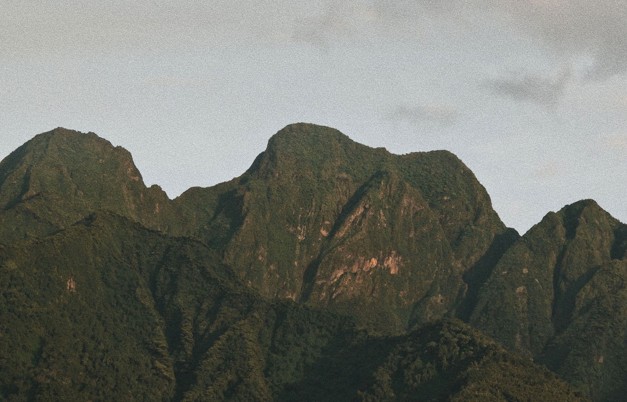 Green mountains under a cloudy sky, showcasing rugged peaks and a densely forested landscape.