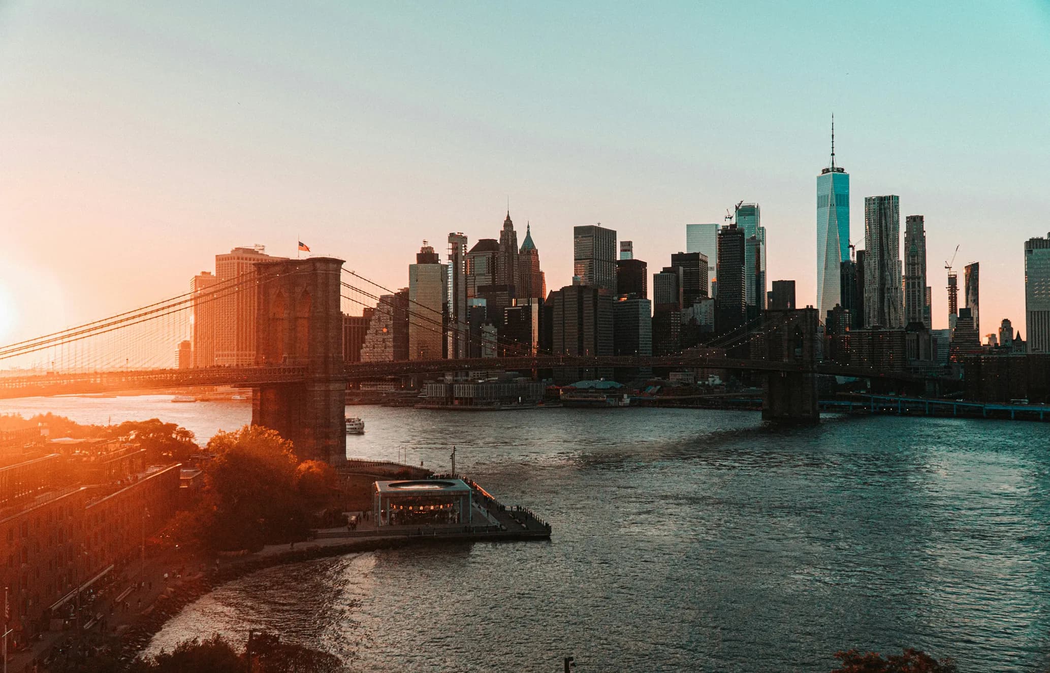 Sunset over the New York City skyline with the Brooklyn Bridge in the foreground, reflecting on the East River.