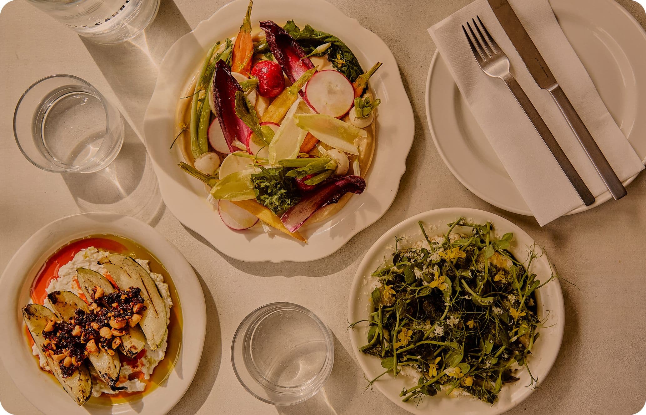 Aerial photo of three plates of food with glasses, napkins and cutlery organised around them.