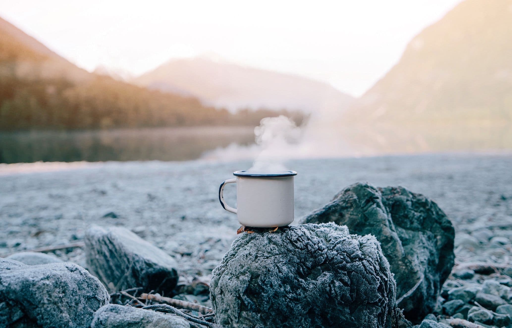 Steam rises from a hot drink on a frosty rock