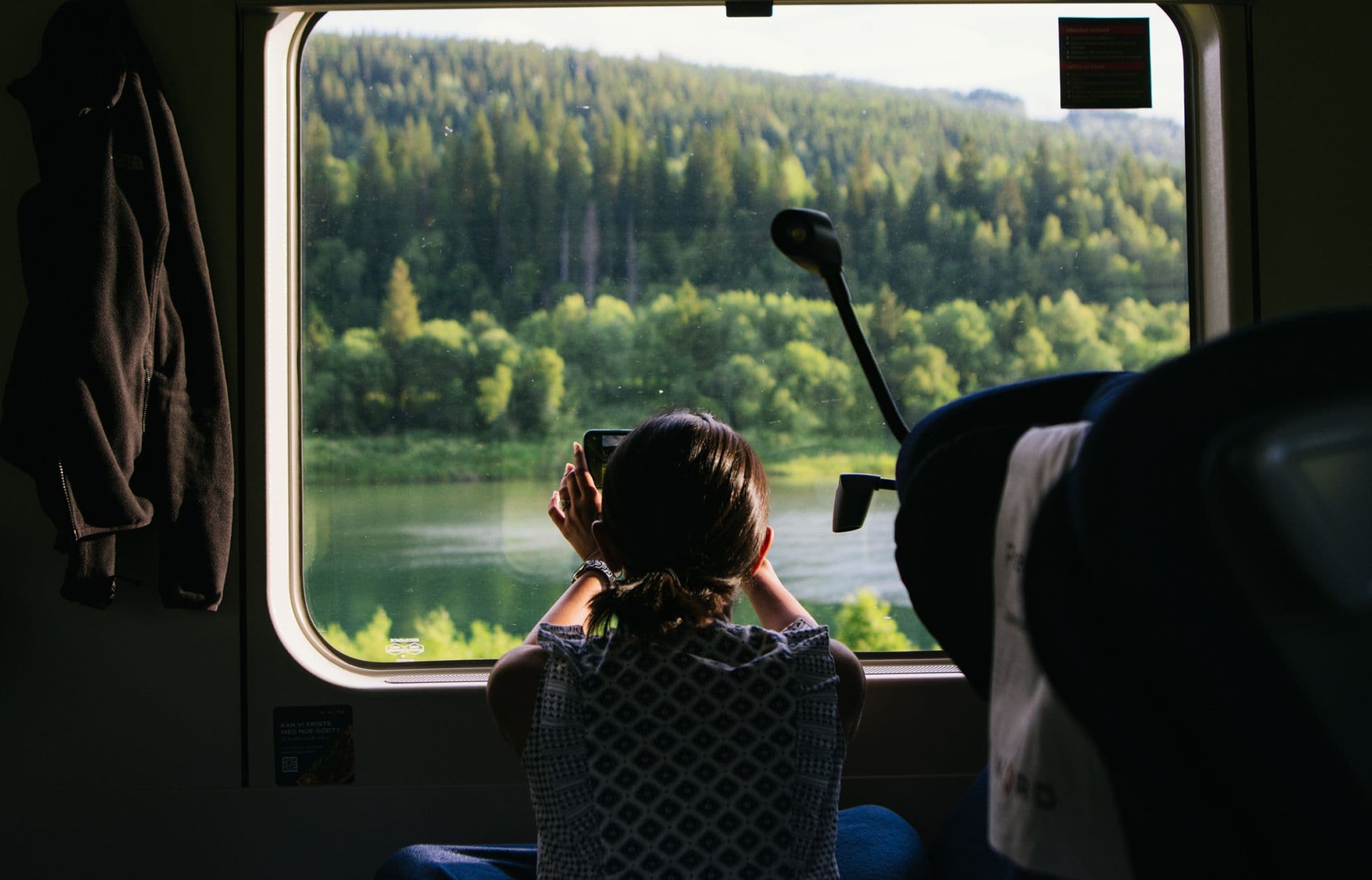 Woman takes photo through the window of a train with lush green and lake views