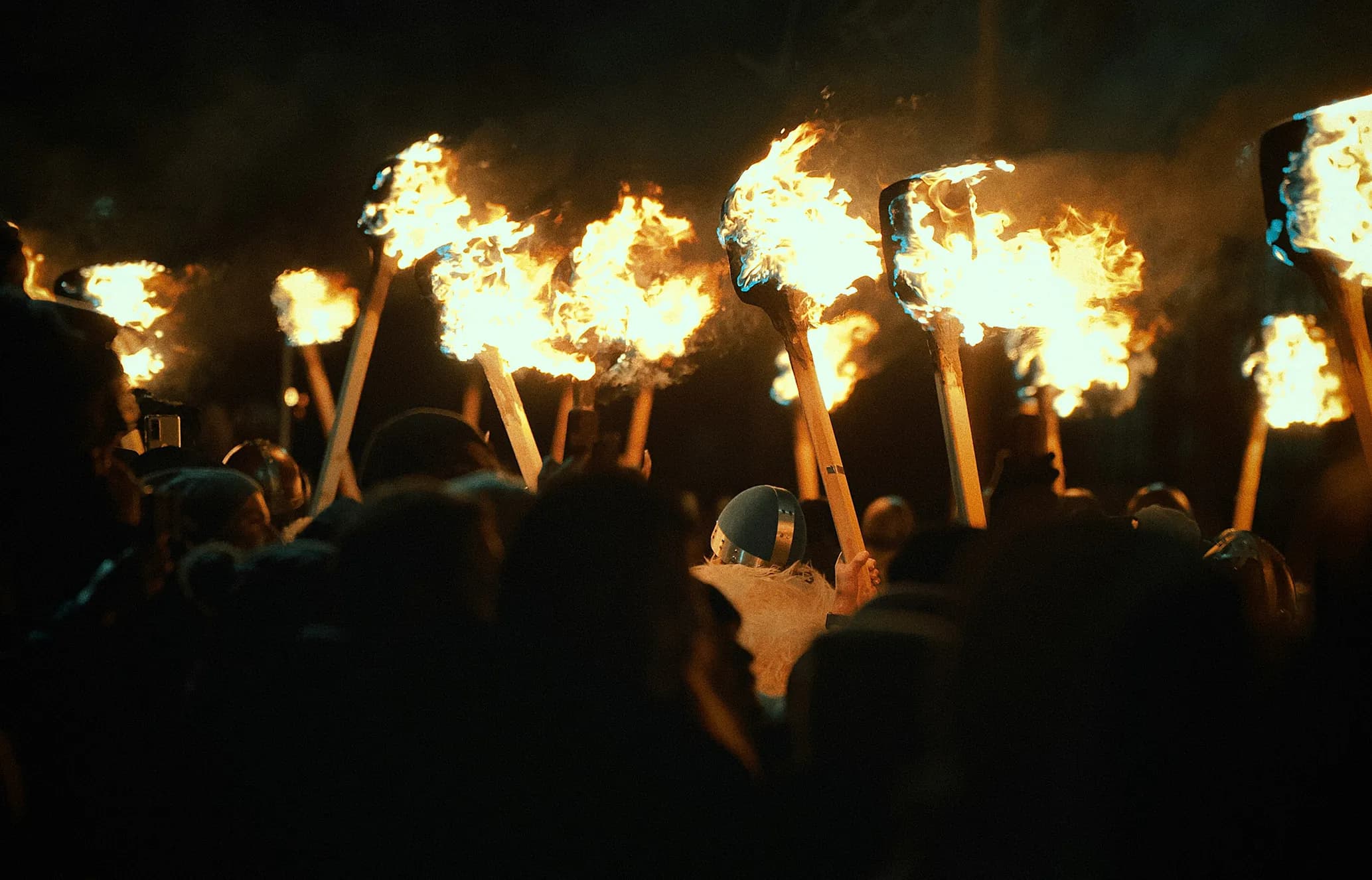 A crowd holding up flaming torches during a dark, night-time event.