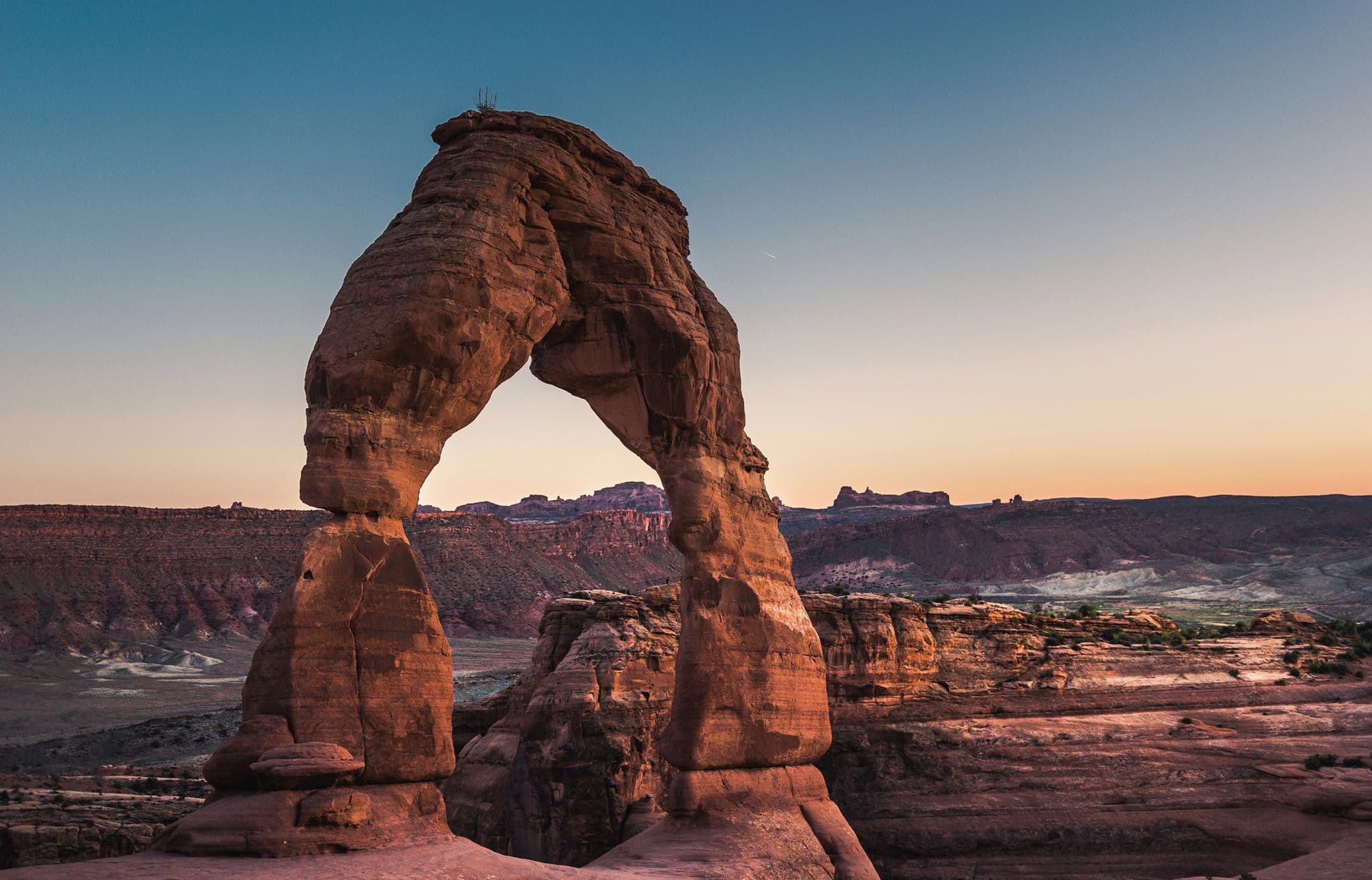 Delicate Arch at sunset, set against a vast desert landscape with a clear sky, showcasing the natural beauty of Arches National Park.