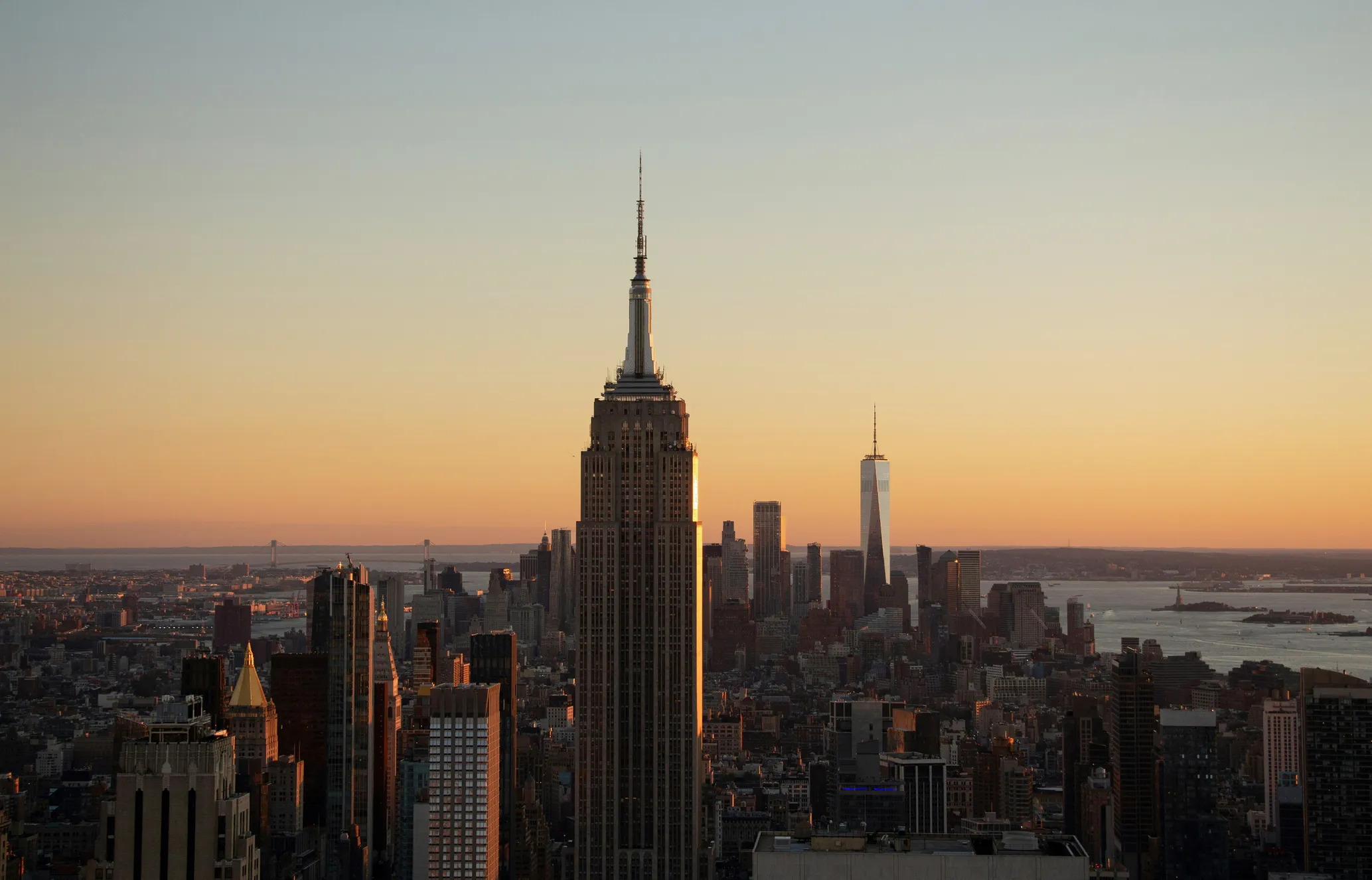 New York City skyline at sunset with prominent skyscrapers silhouetted against an orange sky.