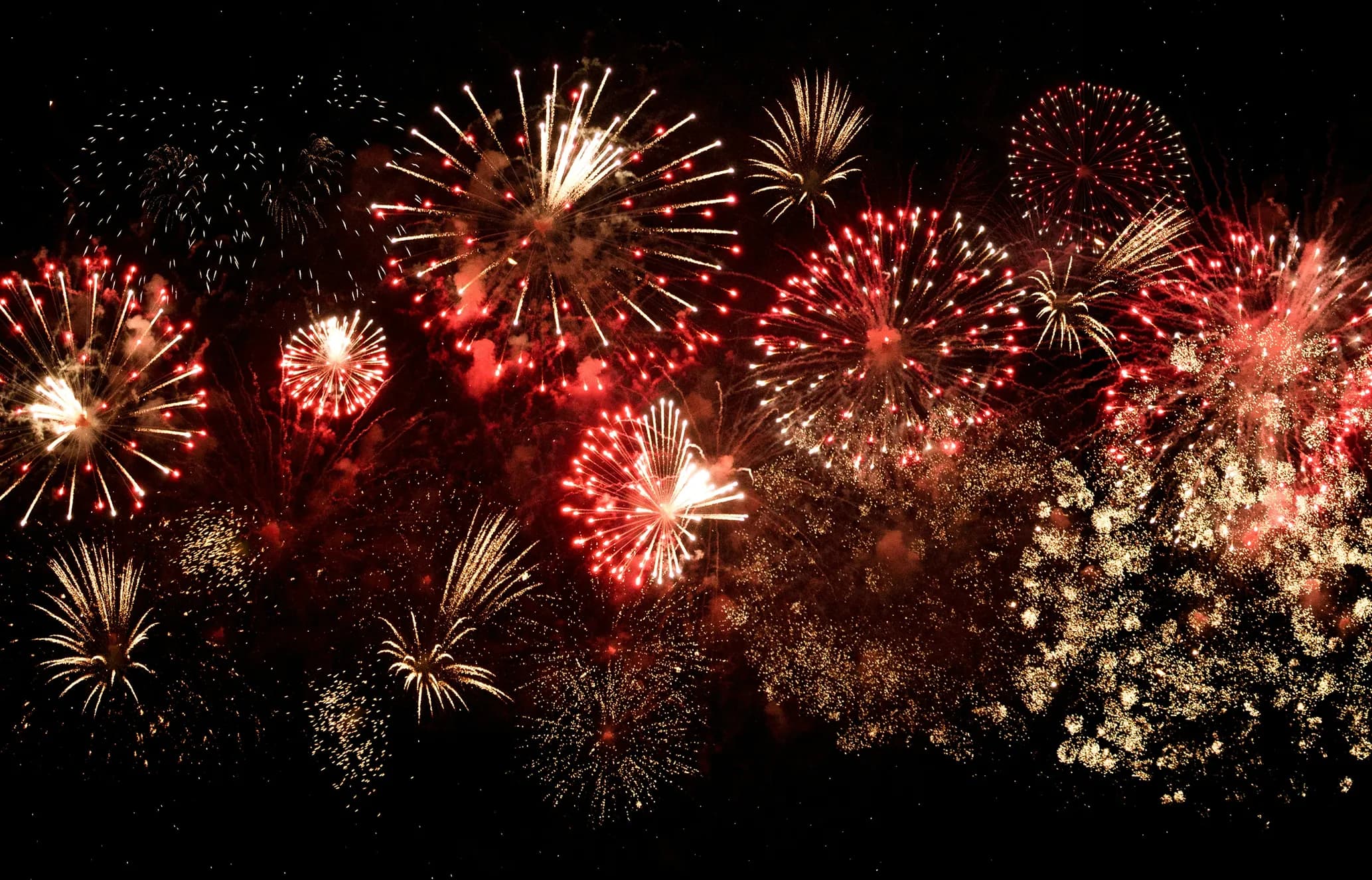 Bright, colorful fireworks with red and gold bursts illuminate the night sky, creating a festive display.
