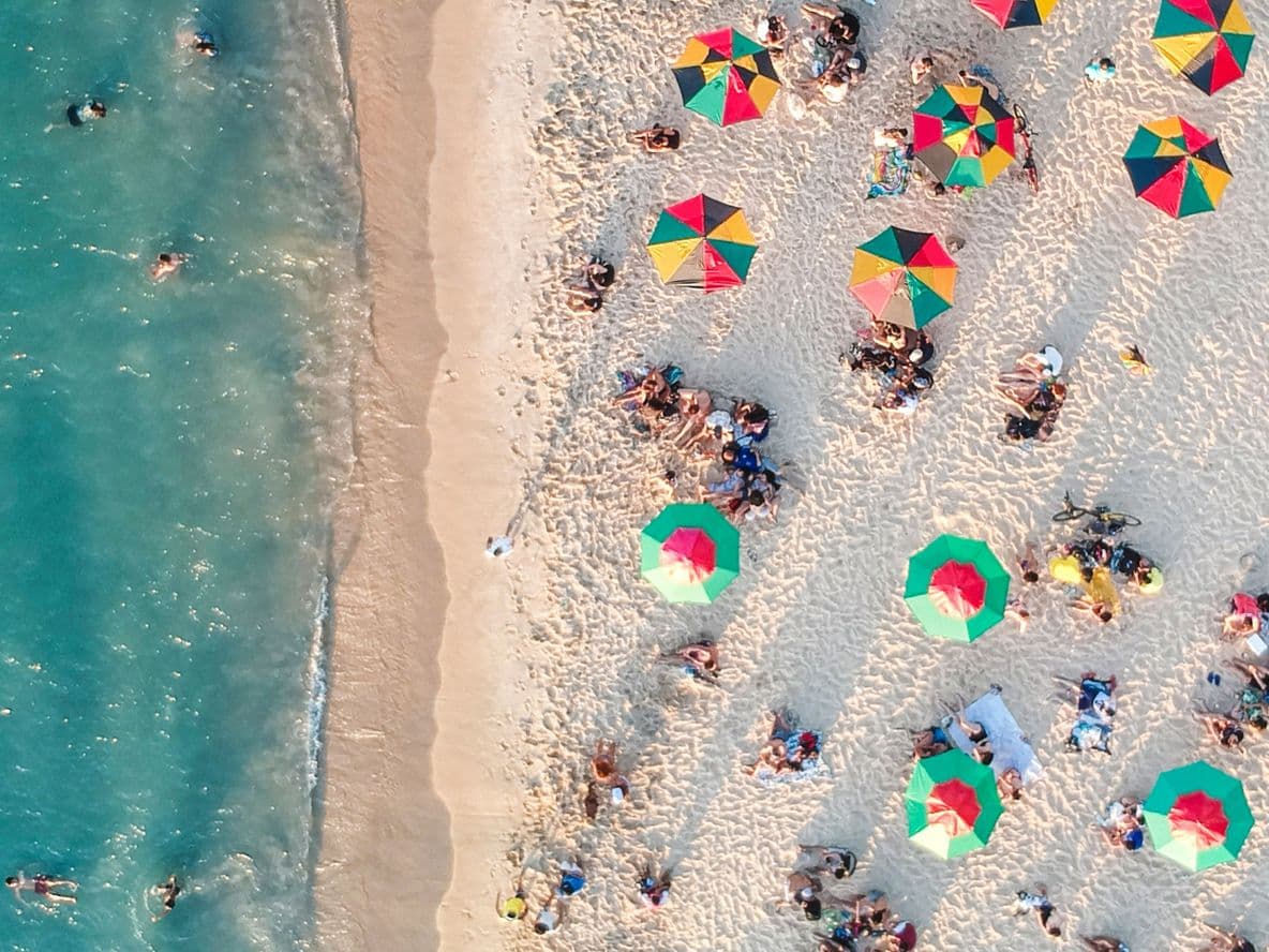 Bird's eye view of sandy beach with holidaymakers sunbathing and playing in the sea