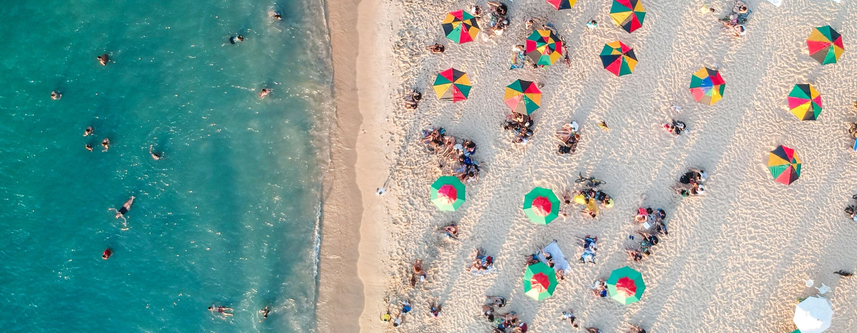 Bird's eye view of sandy beach with holidaymakers sunbathing and playing in the sea
